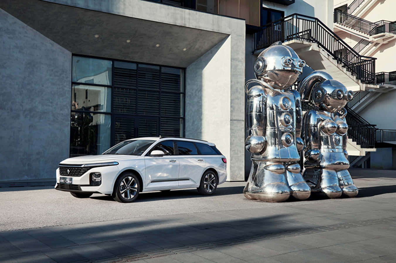 Baojun 桌布 壁紙 — 一輛時尚的白色旅行車停泊在閃亮的鉻合金機器人雕塑旁邊，前面是一座現代混凝土建築。