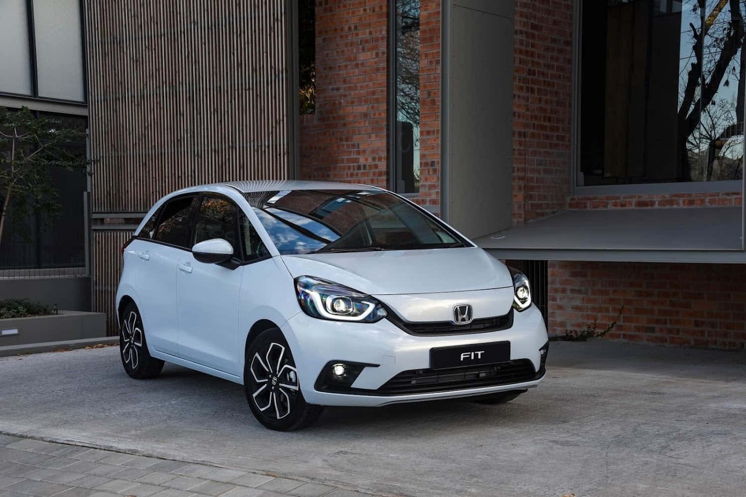 Honda Fit 桌布 壁紙 — 一輛時尚的白色本田Fit停放在鋪砌的庭院旁，旁邊是一座現代磚木建築。