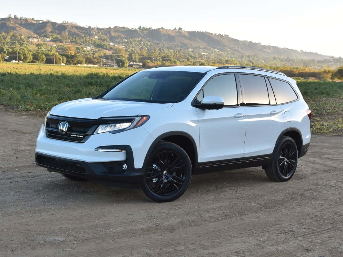 Honda Pilot 桌布 壁紙 — 一輛時尚的白色本田Pilot SUV，配黑色輪圈，停在泥土上，附近是起伏的綠色山丘，光線柔和。