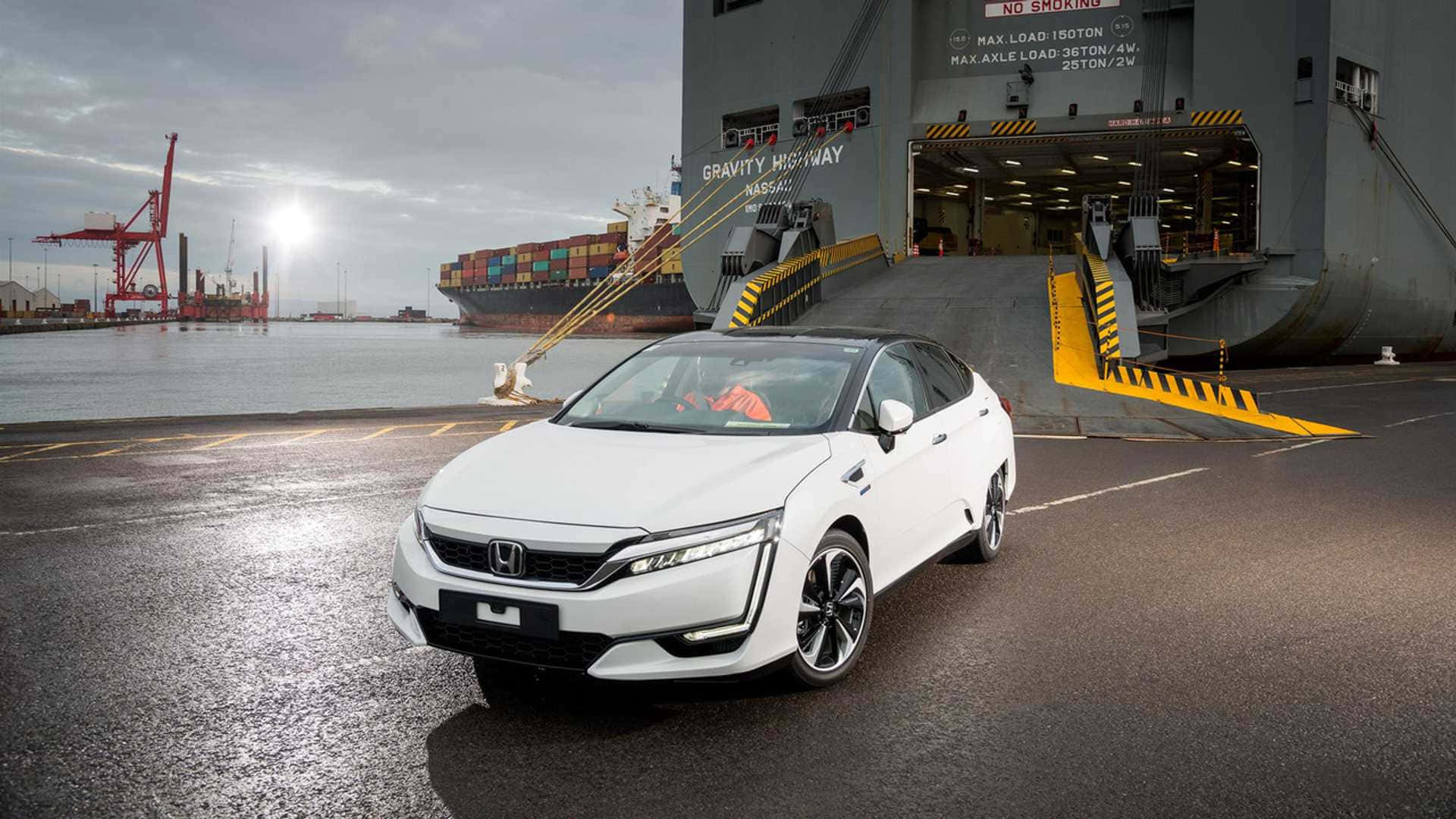 Honda Clarity 桌布 壁紙 — 一輛時尚的白色本田轎車停放在濕滑的碼頭上，旁邊是一艘巨大的貨船，背景有起重機，天空多雲。