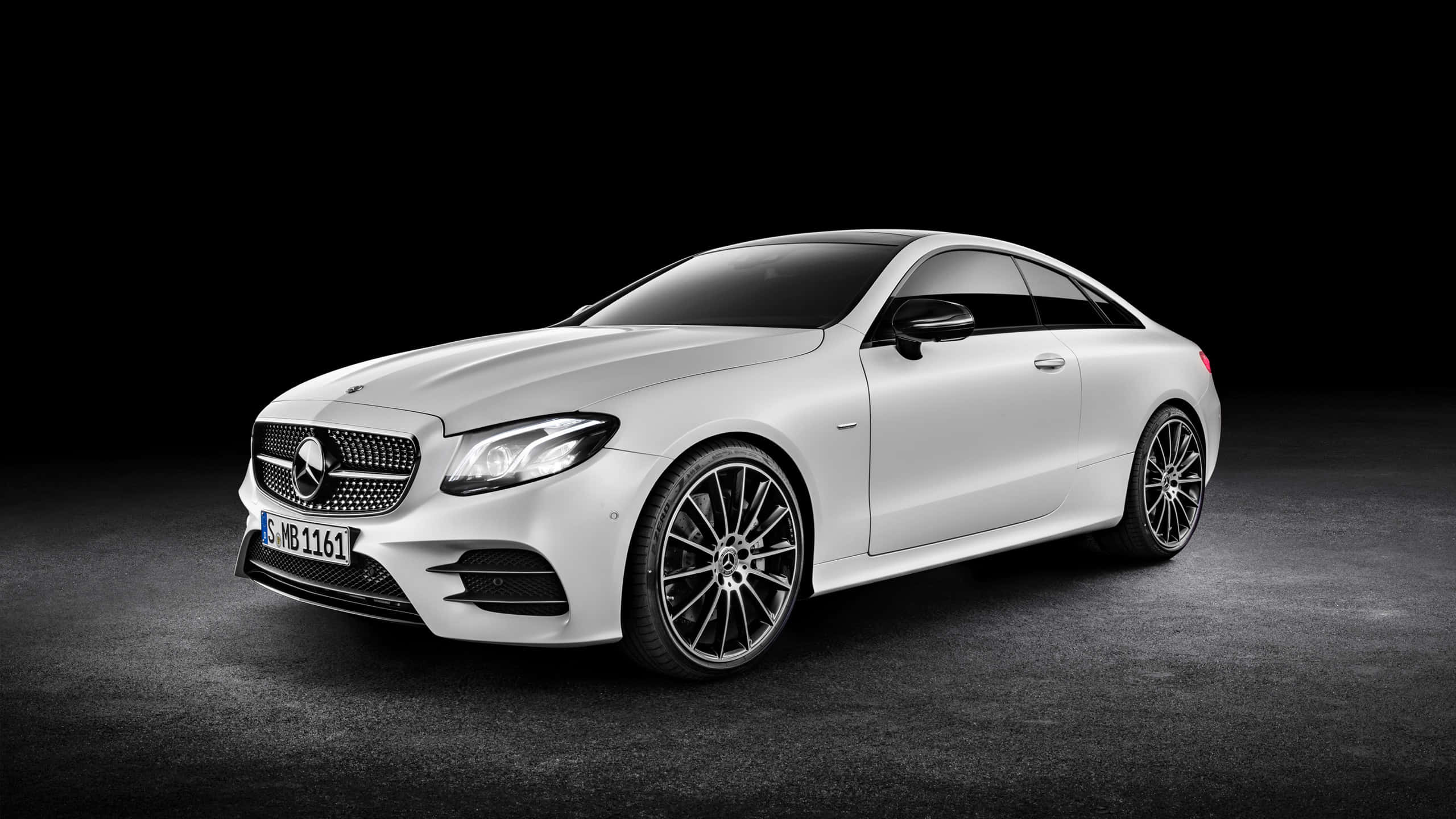 Mercedes Benz Clase E 桌布 壁紙 — 一輛時尚的白色梅賽德斯-奔馳E級轎跑車在攝影棚燈光下閃耀，襯托著純黑背景。