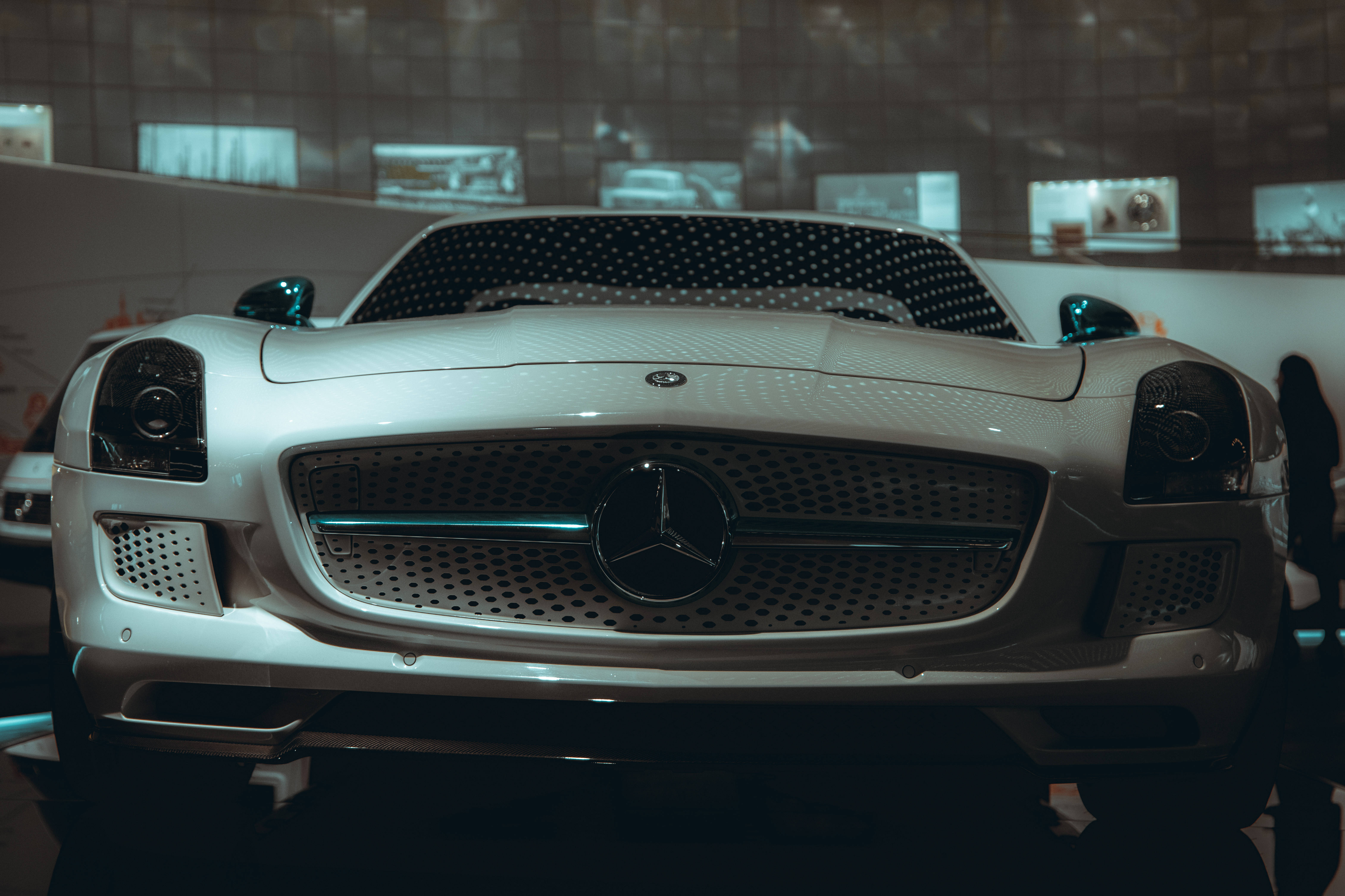 benz 4K 桌布 壁紙 — 一輛時尚的白色梅賽德斯跑車，帶有穿孔格柵和發光頭燈，在昏暗的展覽燈光下展示。