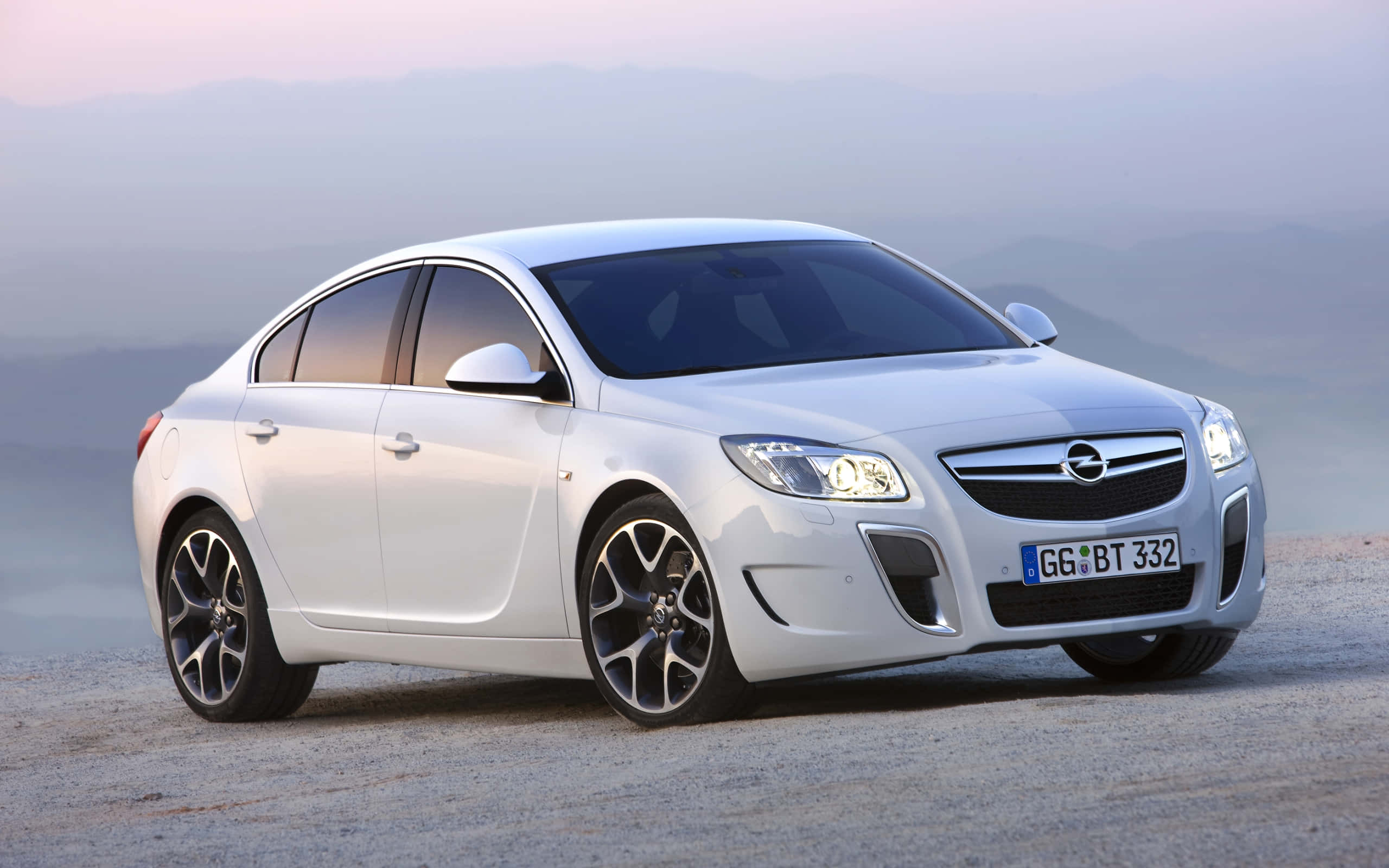 Opel Insignia 桌布 壁紙 — 一輛時尚的白色歐寶Insignia停泊在碎石路上，背景是黎明時分朦朧的山巒。