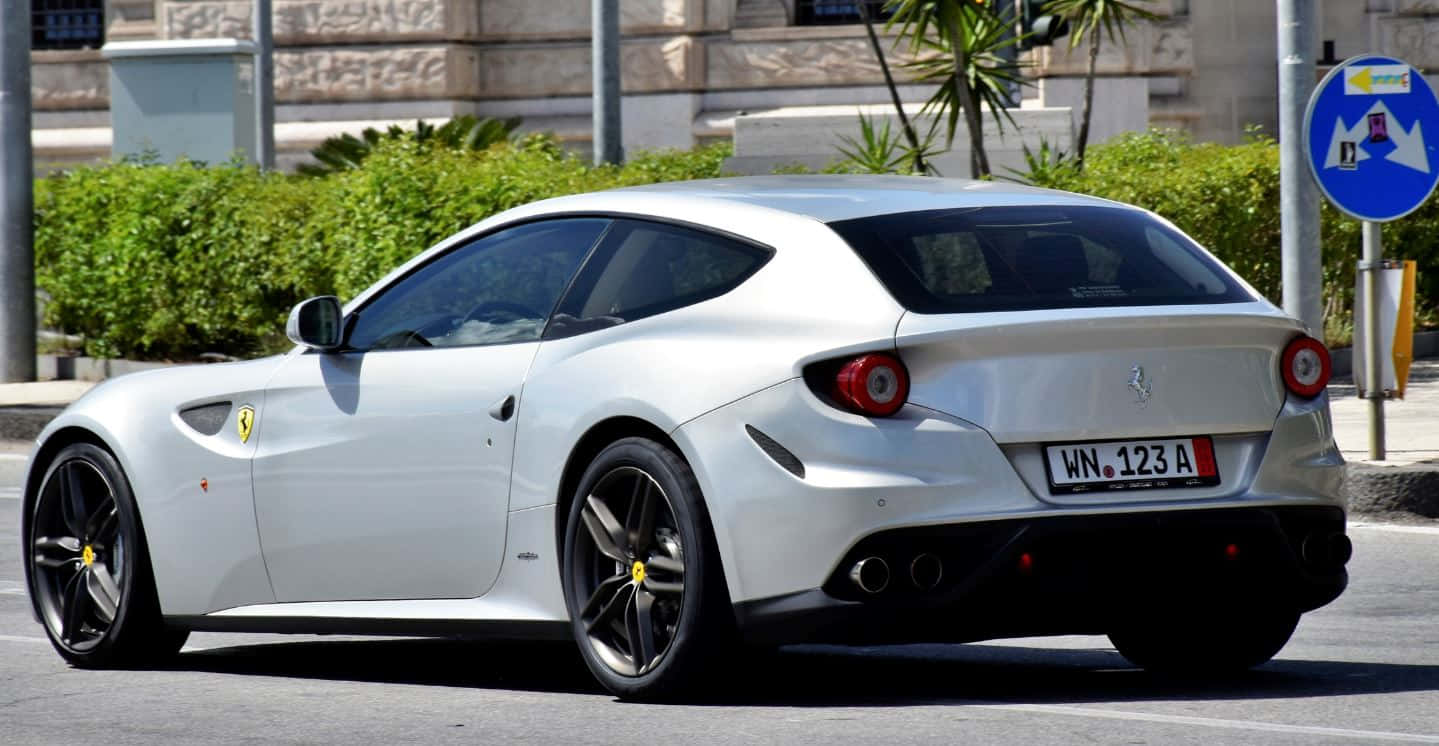 Ferrari Ff 桌布 壁紙 — 一輛時尚的白色法拉利FF跑車停放在陽光明媚的城市街道上，背景有綠色樹籬和石建築。