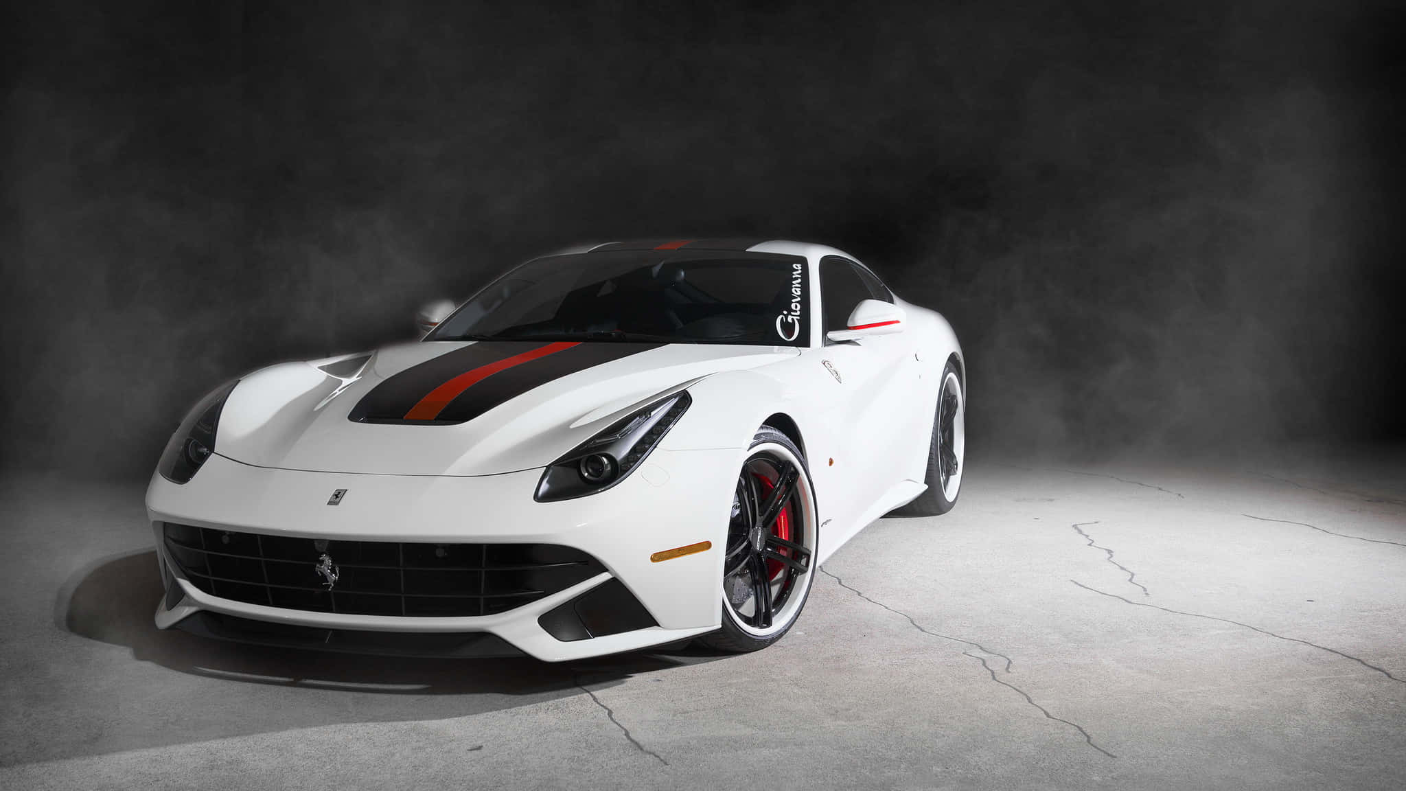 Ferrari F12 Berlinetta 桌布 壁紙 — 一輛時尚的白色法拉利跑車，帶有紅色點綴和黑色賽車條紋，在煙霧瀰漫的黑暗工作室背景下戲劇性地照亮。