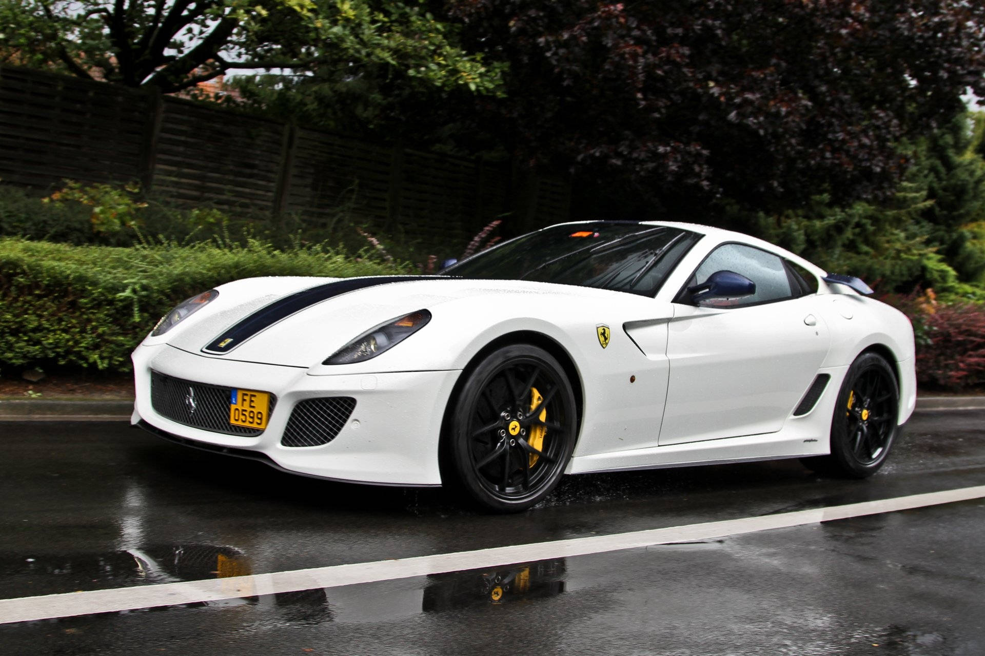 white ferrari 桌布 壁紙 — 一輛時尚的白色法拉利跑車，帶有黑色飾邊和黃色制動卡鉗，停在潮濕的道路上，反射出其光澤的表面。