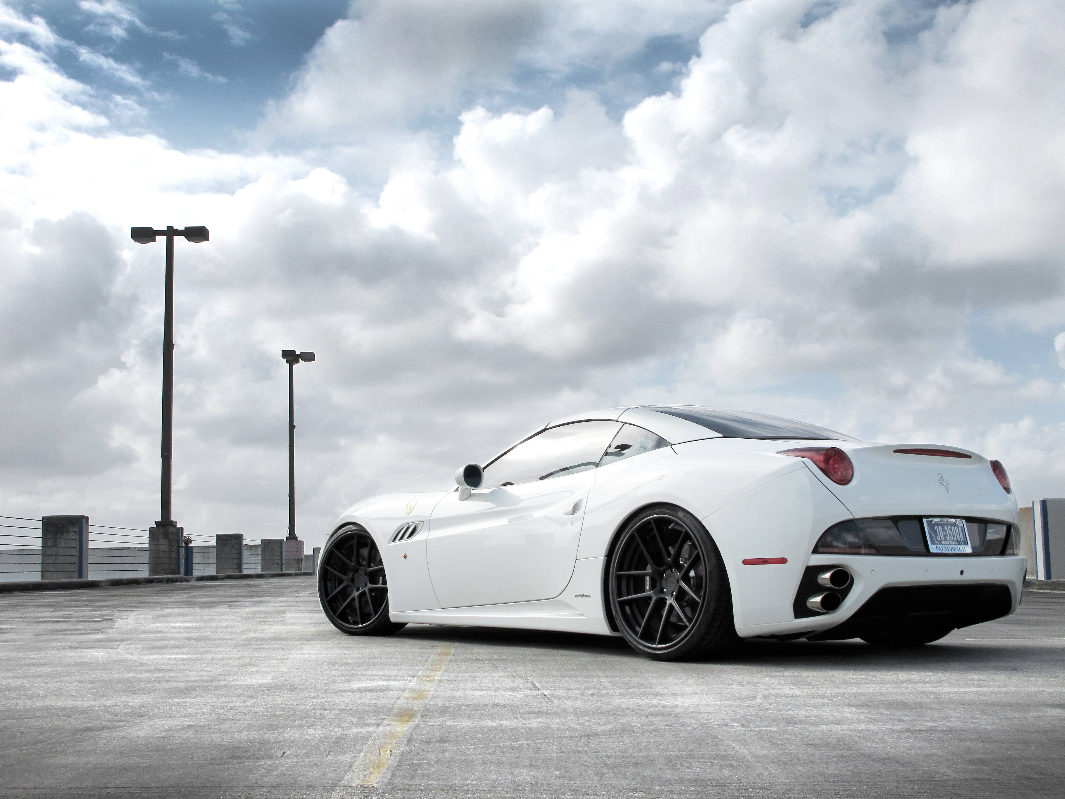 white ferrari 桌布 壁紙 — 一輛時尚的白色法拉利跑車，配黑色輪圈，停泊在混凝土天台上，天空多雲。