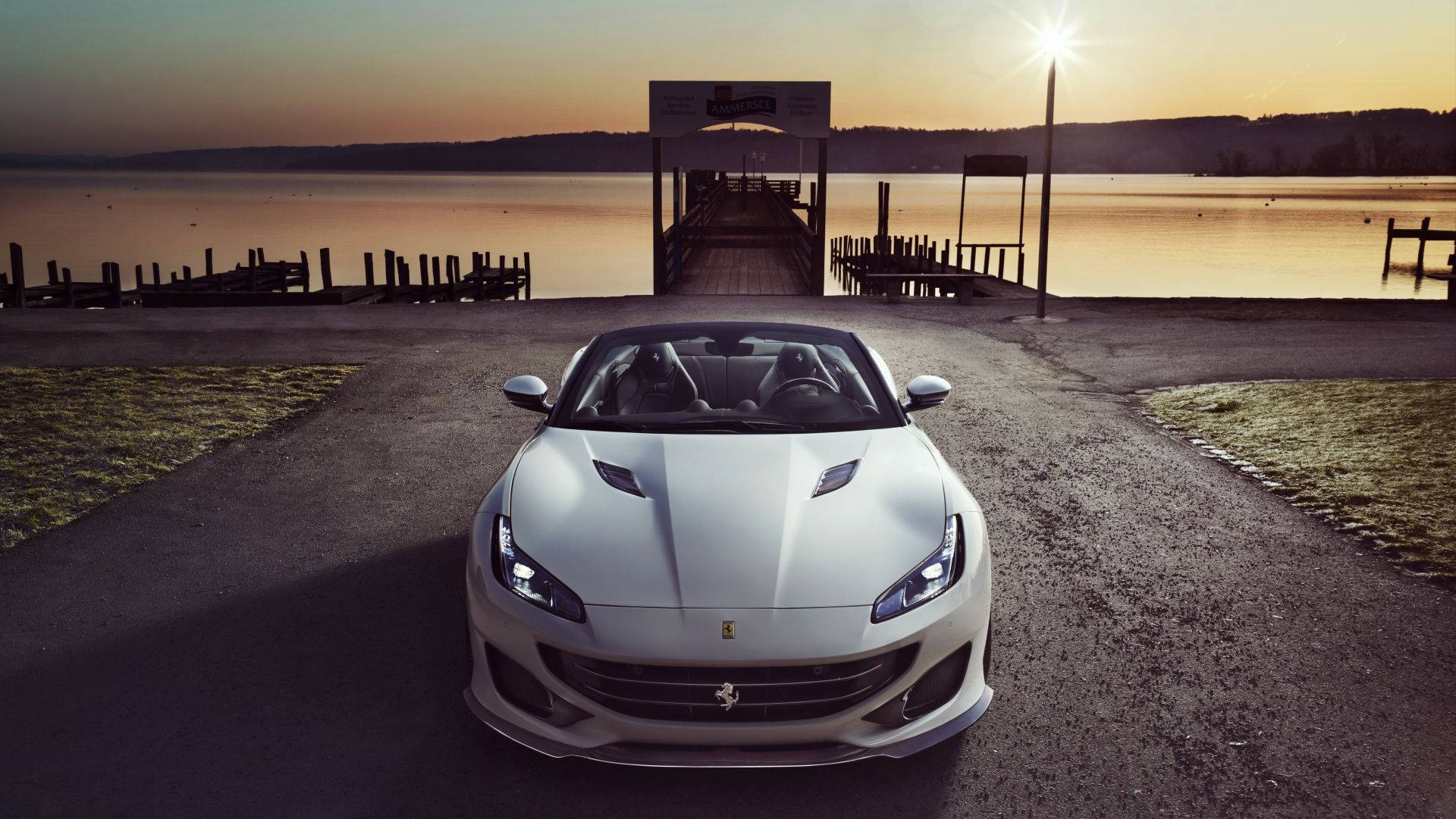 white ferrari 桌布 壁紙 — 一輛時尚的白色法拉利跑車停在湖邊道路上，夕陽西下，木製碼頭延伸至平靜的水面。