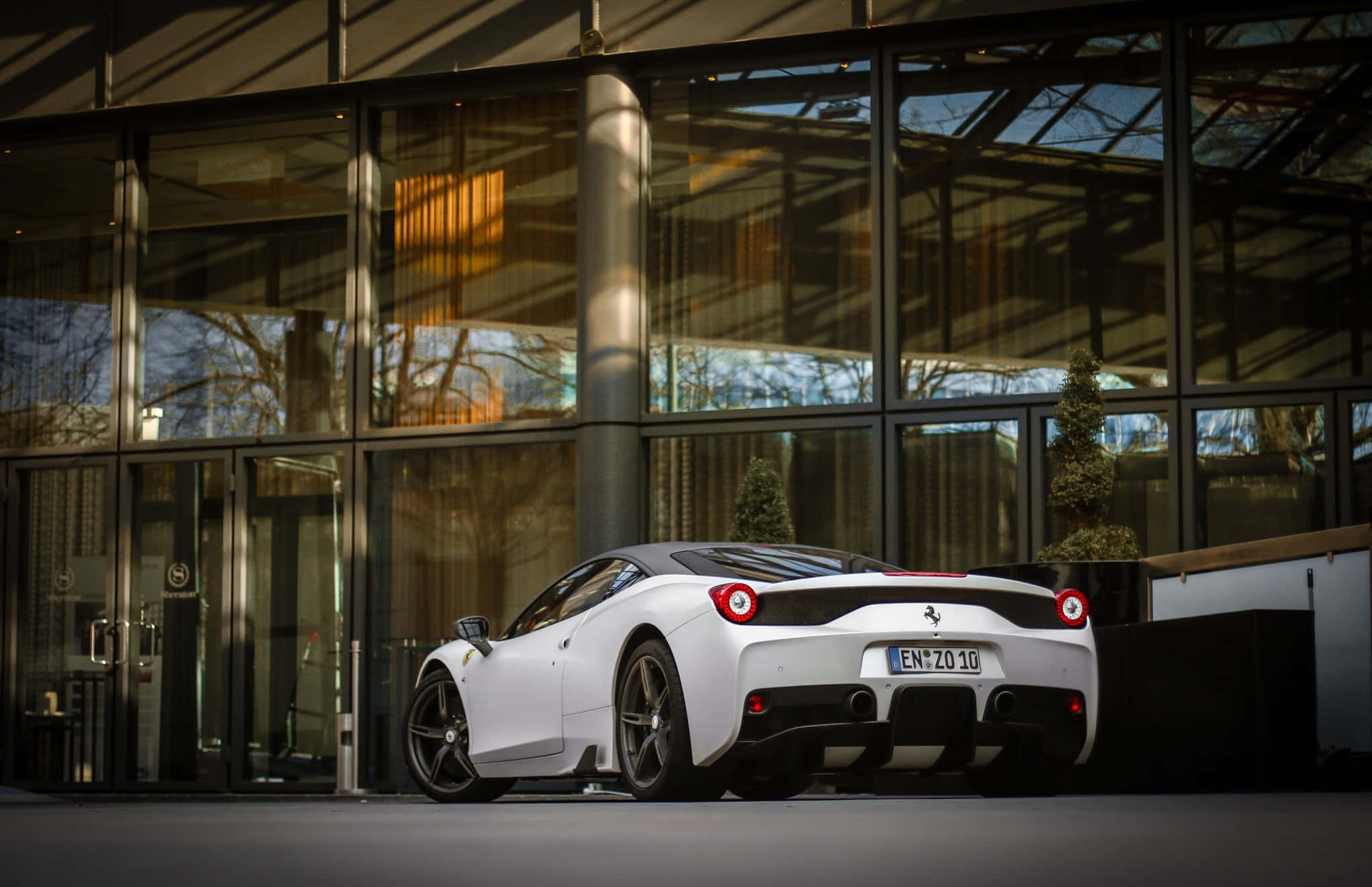 Ferrari 458 Speciale 桌布 壁紙 — 一輛時尚的白色法拉利跑車停放在現代玻璃建築外，陽光投射出溫暖的反射。