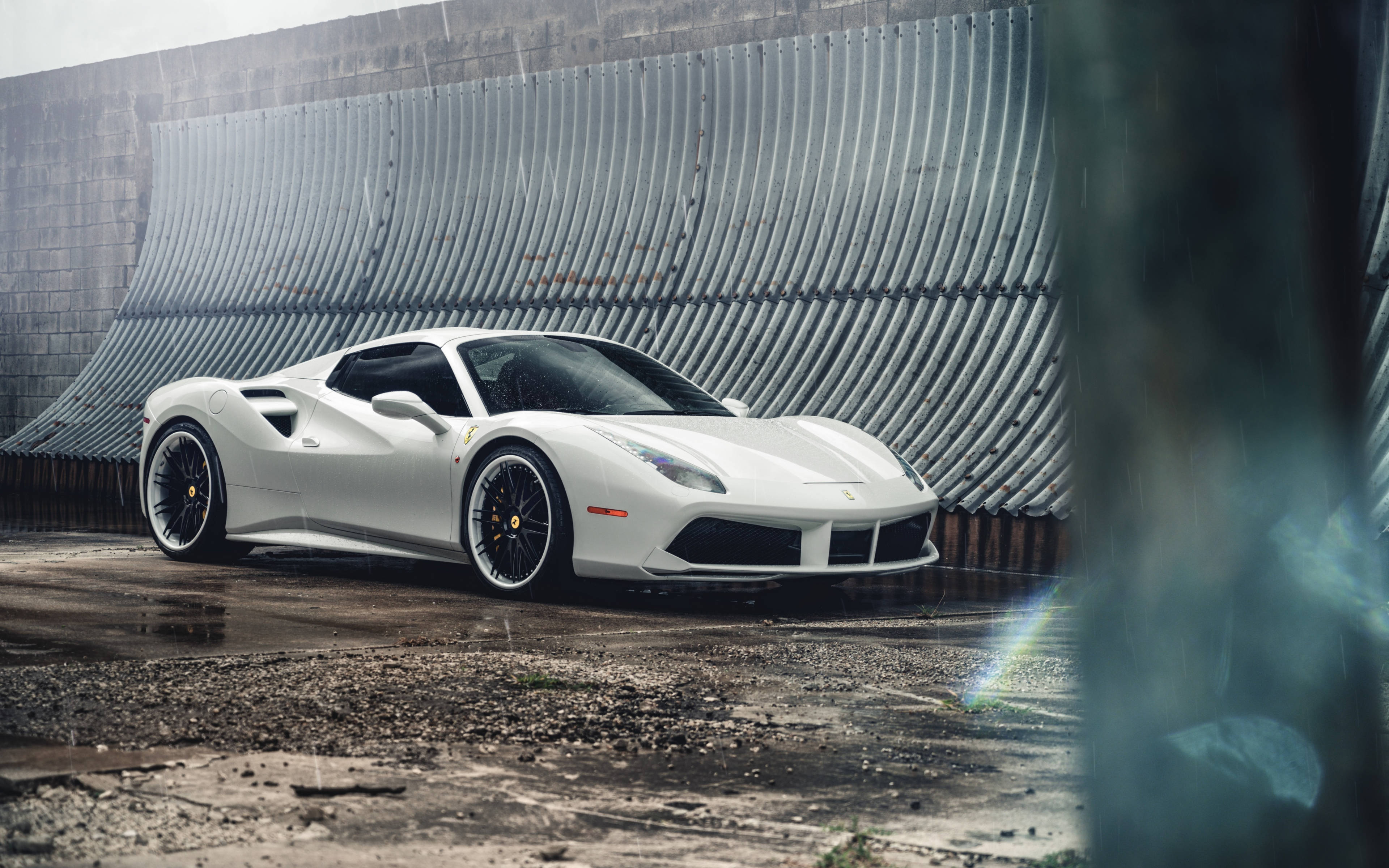 white ferrari 桌布 壁紙 — 一輛時尚的白色法拉利跑車停泊在濕漉漉的碎石上，背景是波紋金屬牆，天空多雲。