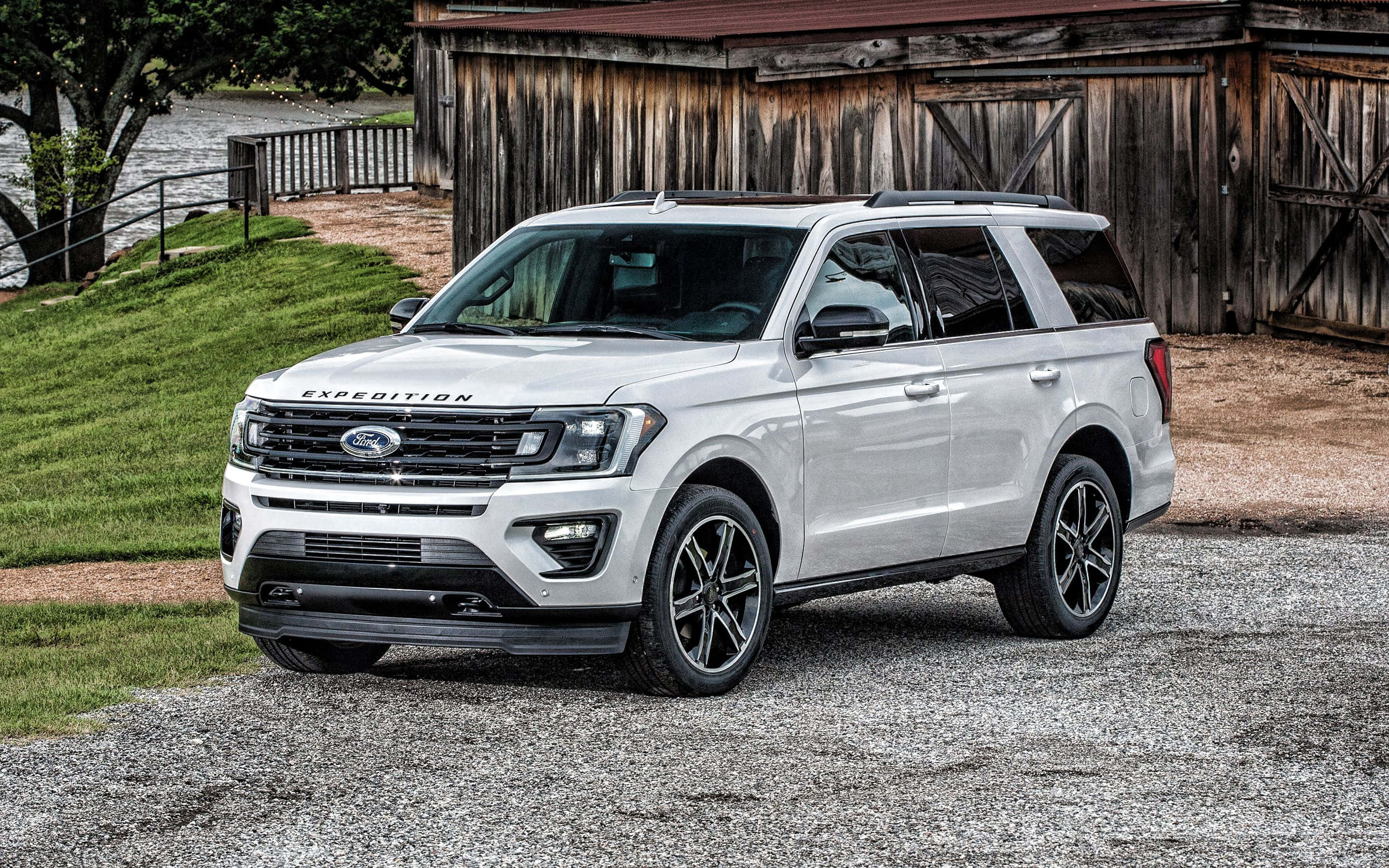 Ford Expedition 桌布 壁紙 — 一輛時尚的白色福特 Expedition SUV 停泊在碎石路上，前面是鄉村風格的木製穀倉，背景有綠草和河流。