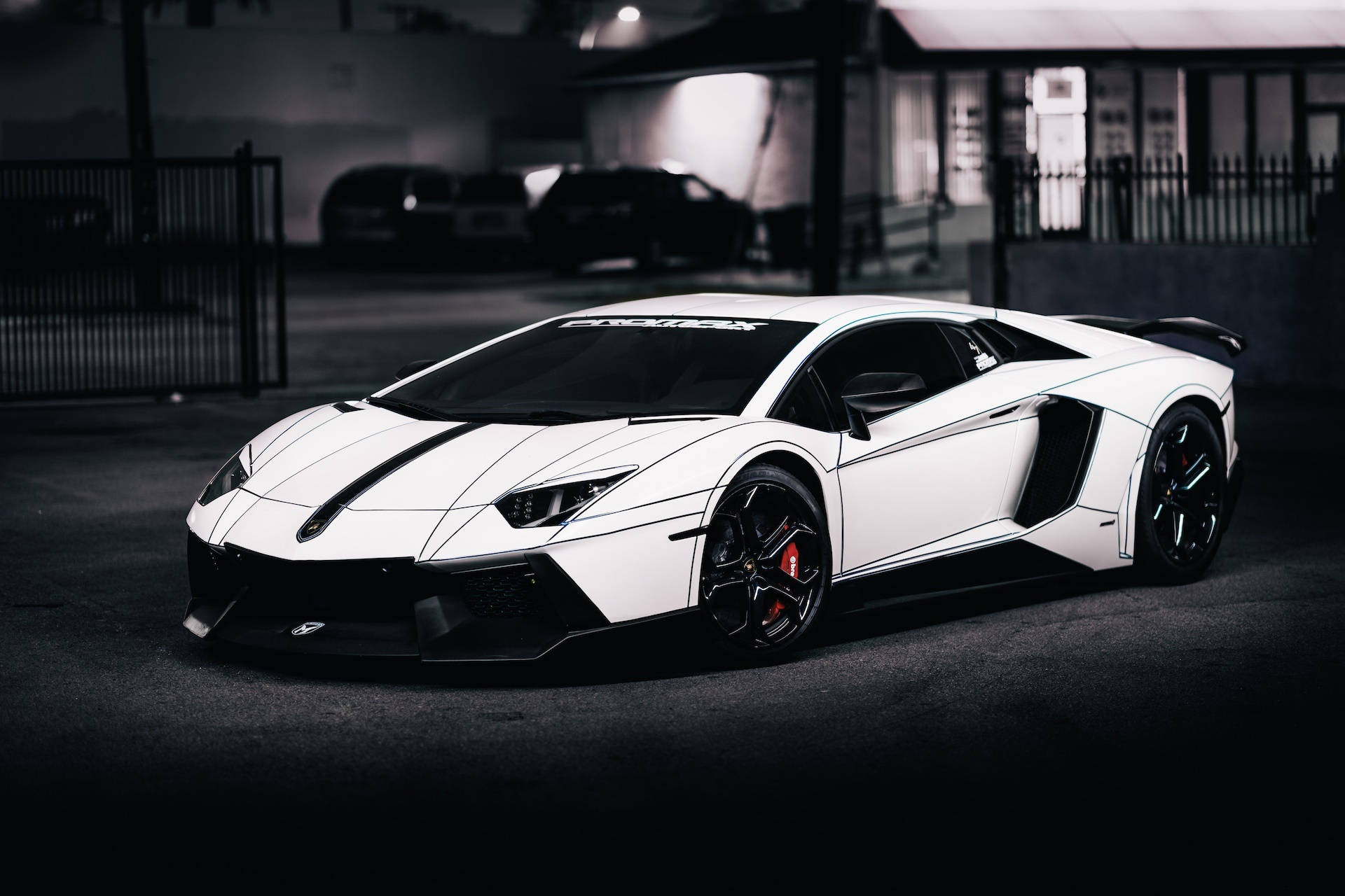 創戰紀 桌布 壁紙 — 一輛時尚的白色藍寶堅尼 Aventador，帶有黑色飾邊和紅色制動卡鉗，停在光線昏暗的城市車庫中。