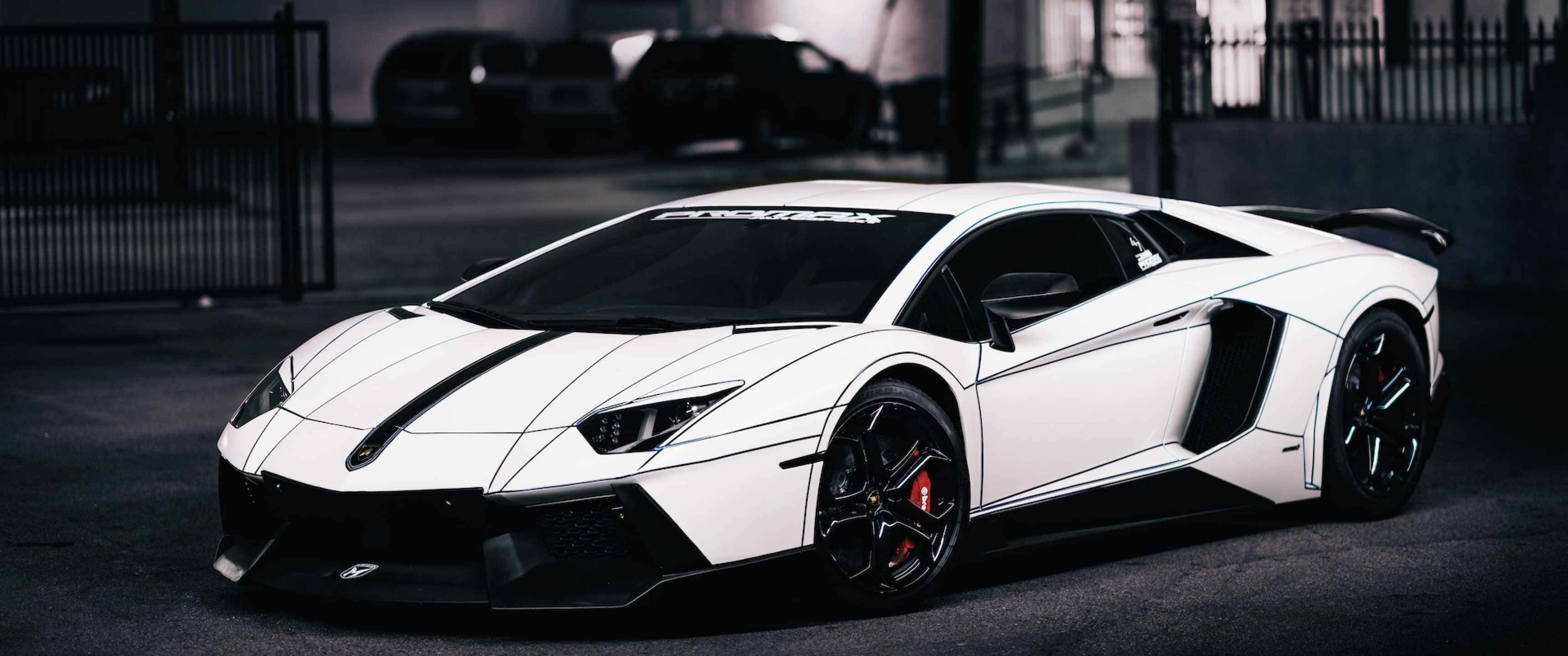 3440x1440p Lamborghini 桌布 壁紙 — 一輛時尚的白色藍寶堅尼Aventador，帶有黑色飾邊和紅色制動卡鉗，停放在光線昏暗的城市車庫中。