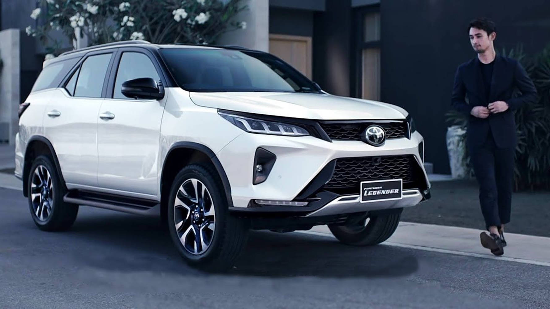 Toyota 桌布 壁紙 — 一輛時尚的白色豐田 Fortuner Legend SUV 停放在現代街道上，附近有一位身穿黑色西裝的男子走過。