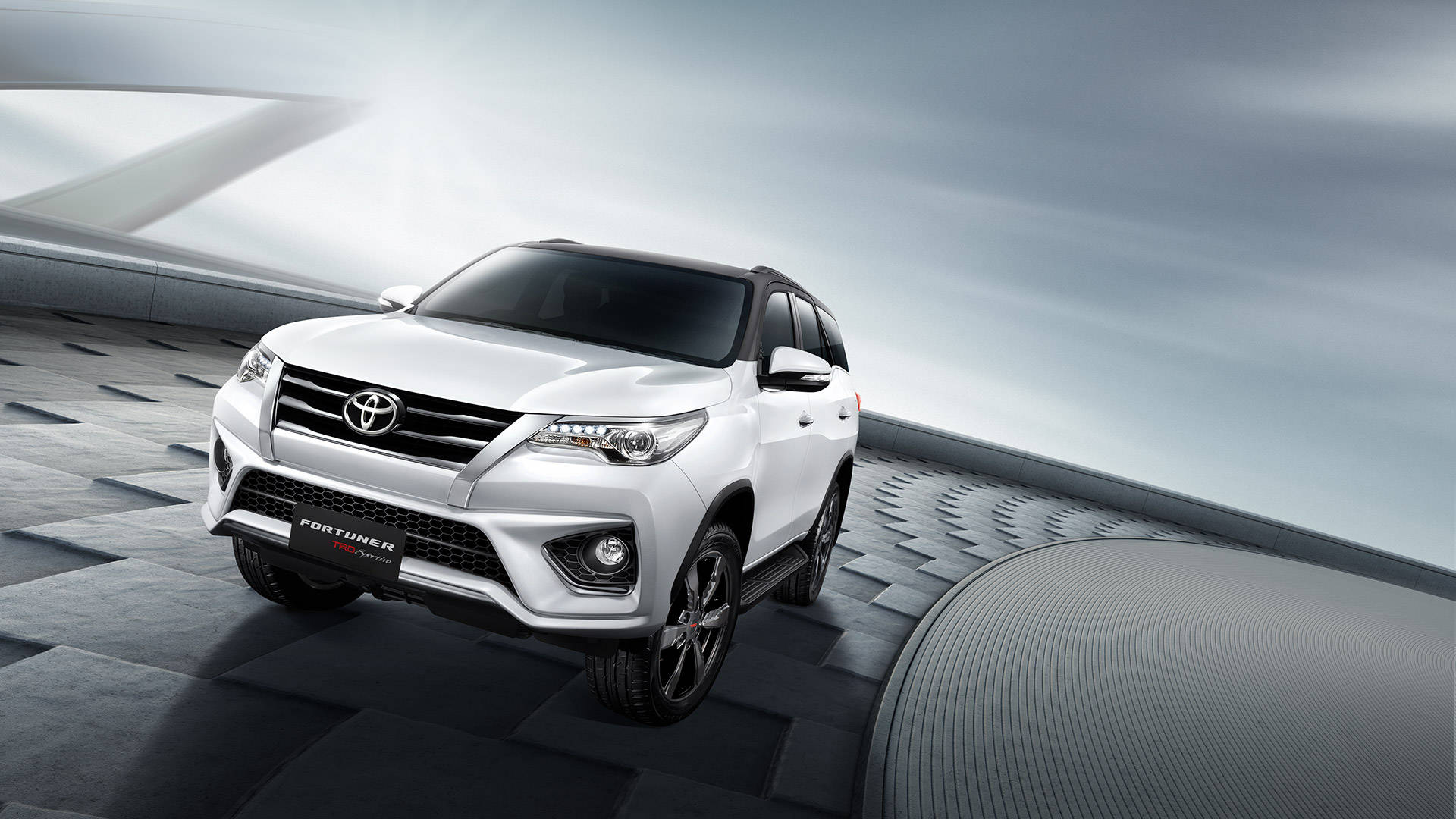 Toyota 桌布 壁紙 — 一輛時尚的白色豐田 Fortuner SUV 停放在現代幾何平台上，天空陰沉灰暗。