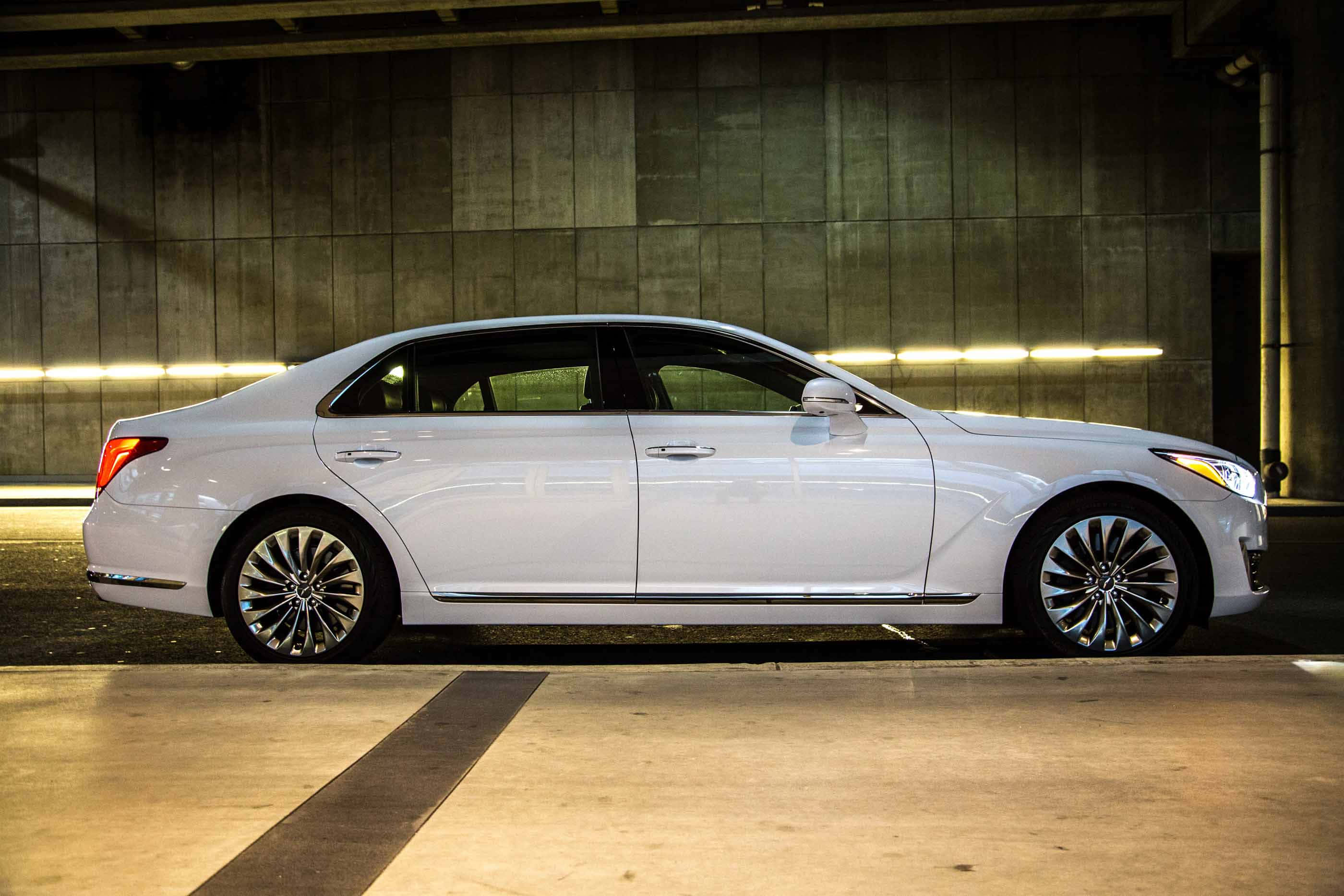 Genesis G90 桌布 壁紙 — 一輛時尚的白色豪華轎車停放在燈光昏暗的地下停車場，周圍是混凝土牆壁和發光的條形燈。