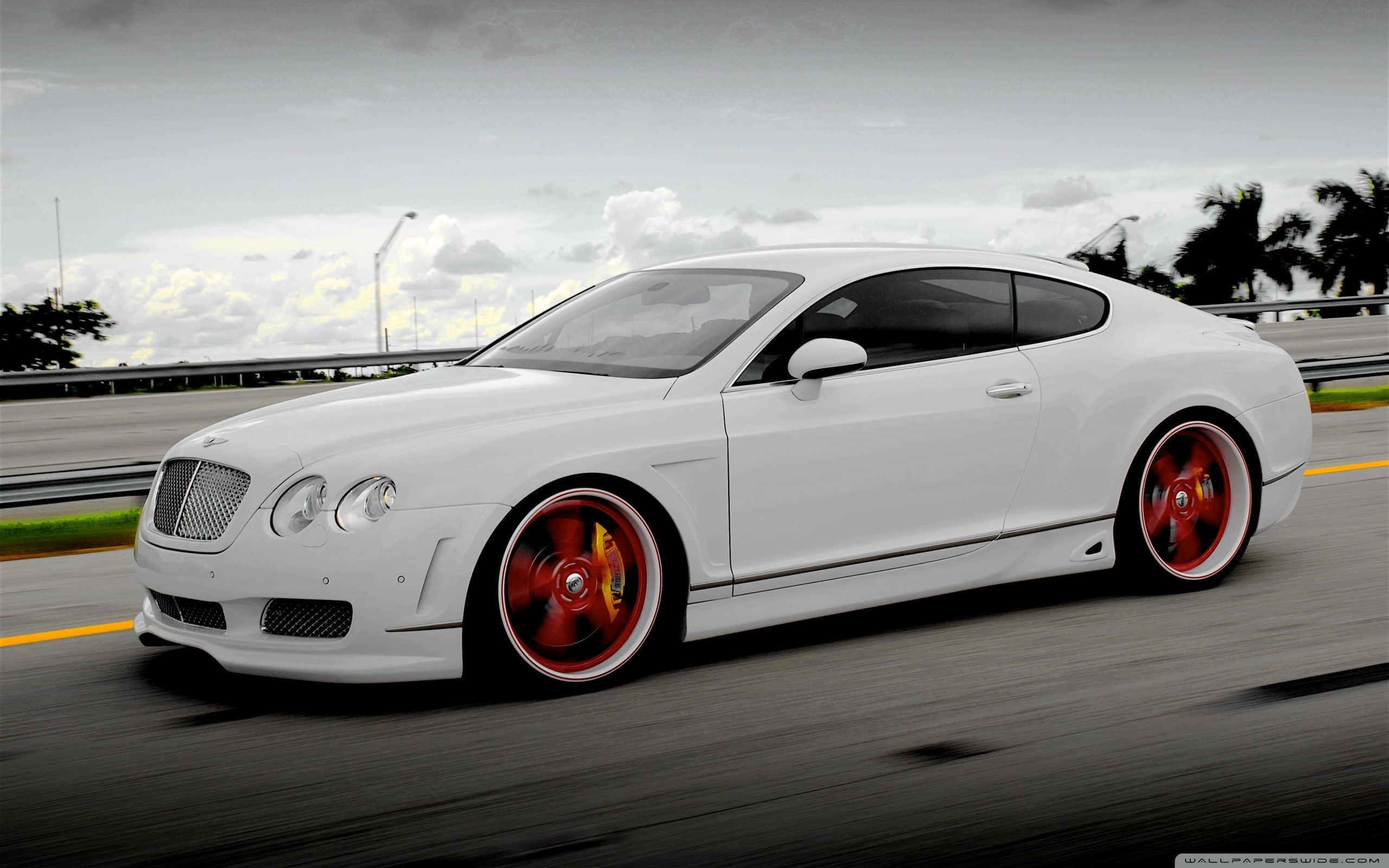 1366x768 Bentley 桌布 壁紙 — 一輛時尚的白色賓利 Continental GT 在陰天的高速公路上疾馳，配以鮮紅色的車輪。