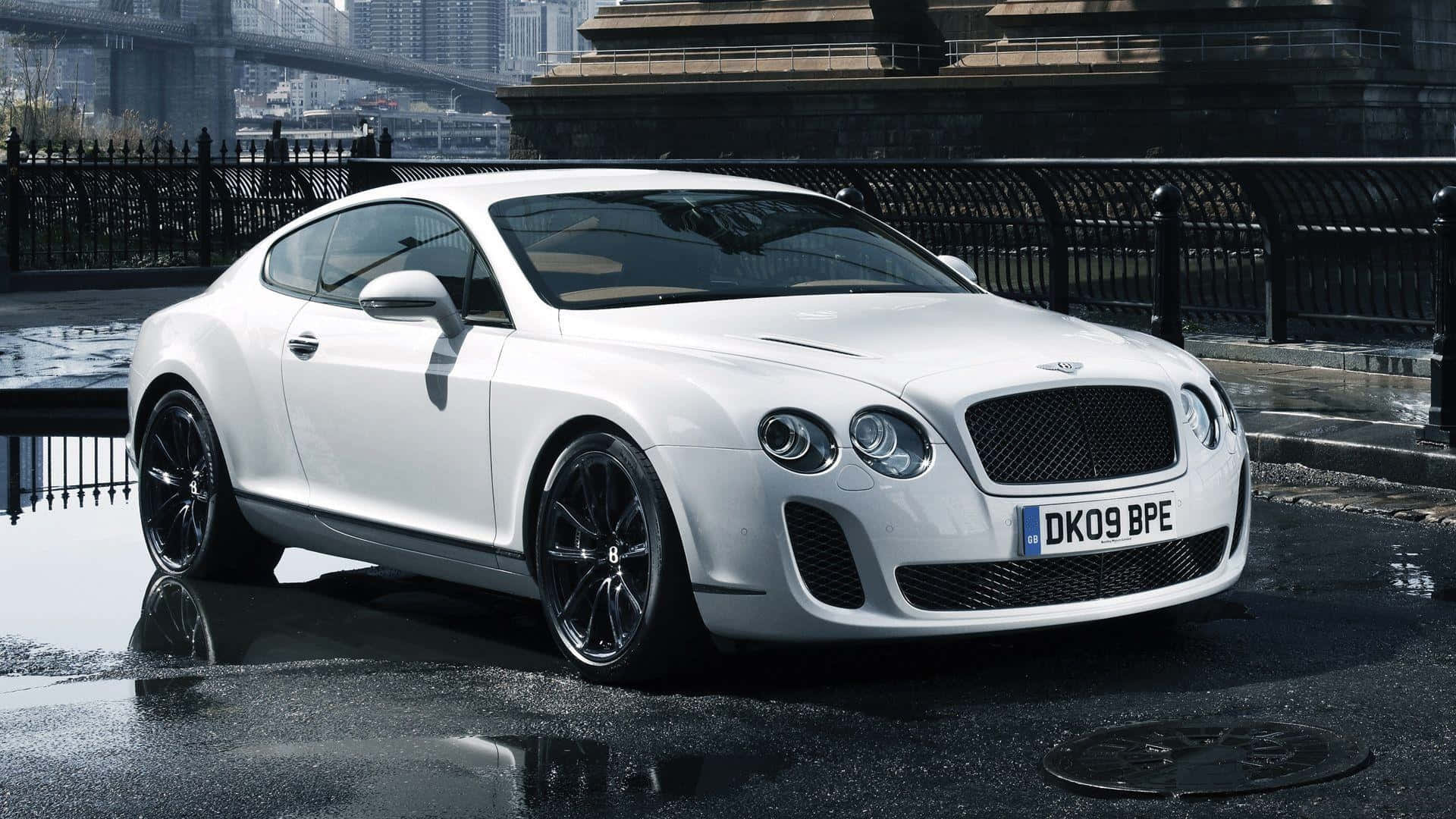 桌布 壁紙 — 一輛時尚的白色賓利 Continental GT 雙門跑車在城市燈光下，在濕漉漉的路面上閃閃發光，背景是橋樑和石頭建築。