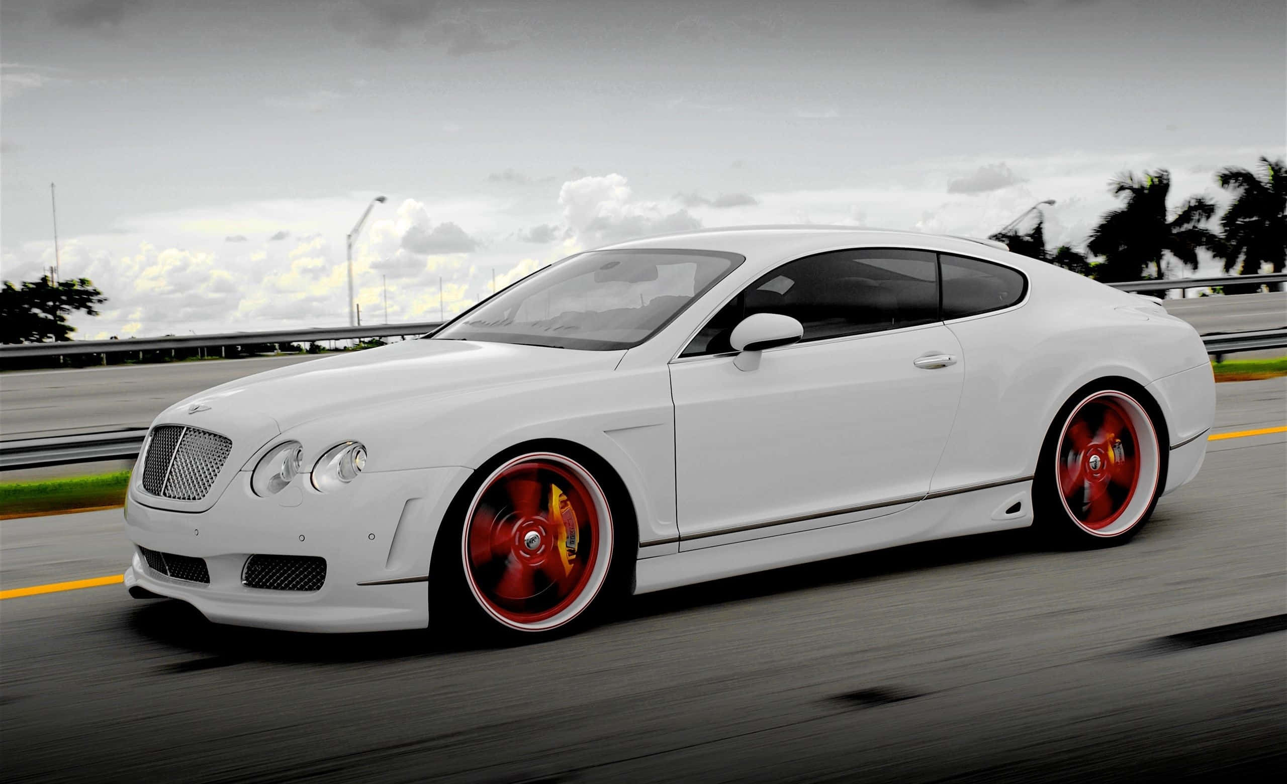 Best Bentley 桌布 壁紙 — 一輛時尚的白色賓利 Continental GT 配以鮮紅色輪圈，在多雲的天空下沿高速公路疾馳。