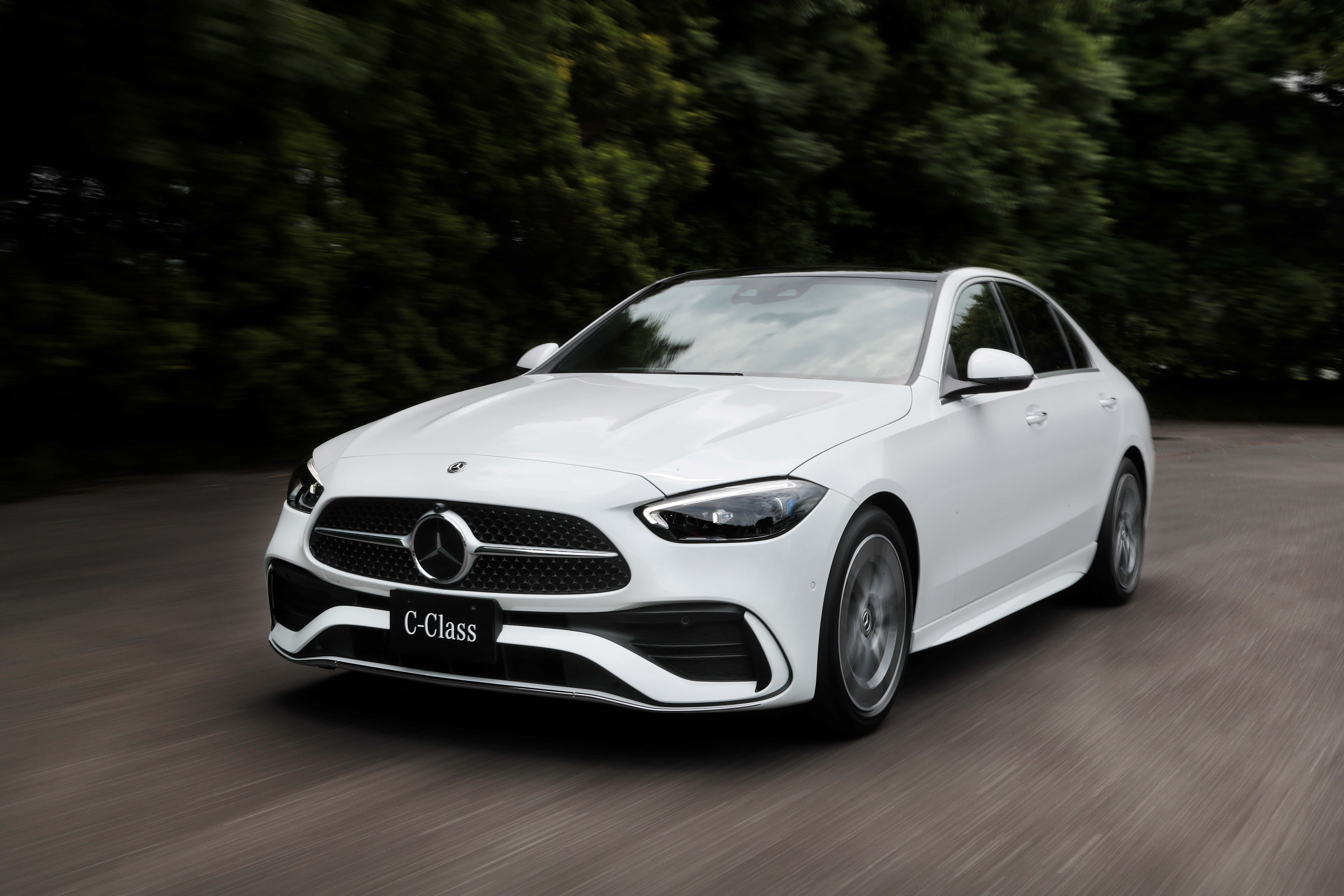 Mercedes Car 4K 桌布 壁紙 — 一輛時尚的白色賓士C-Class轎車在森林道路上行駛，動態模糊強調其動感。