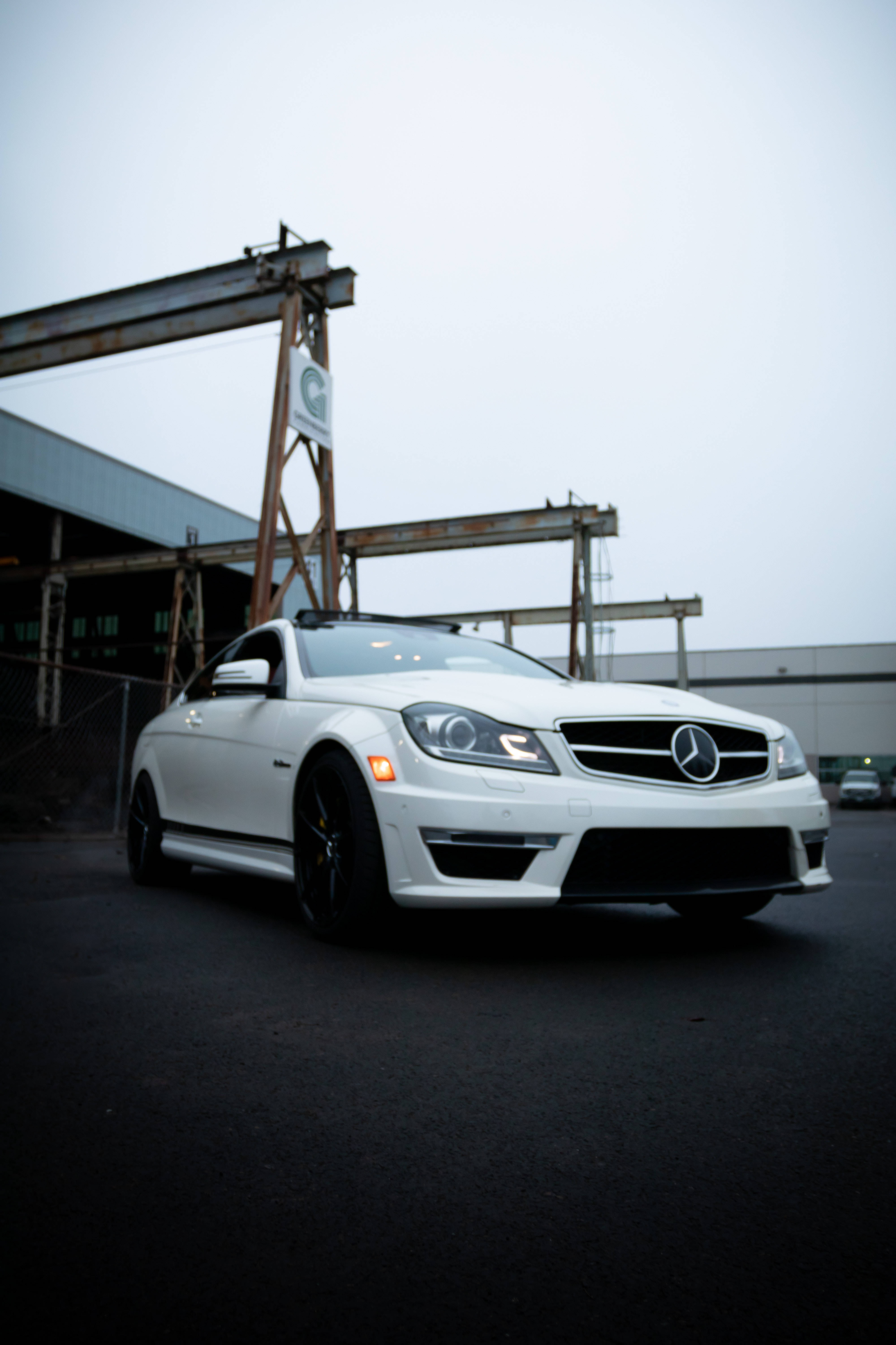 mercedes amg iPhone 桌布 壁紙 — 一輛時尚的白色賓士跑車停放在工業起重機前，天空多雲。