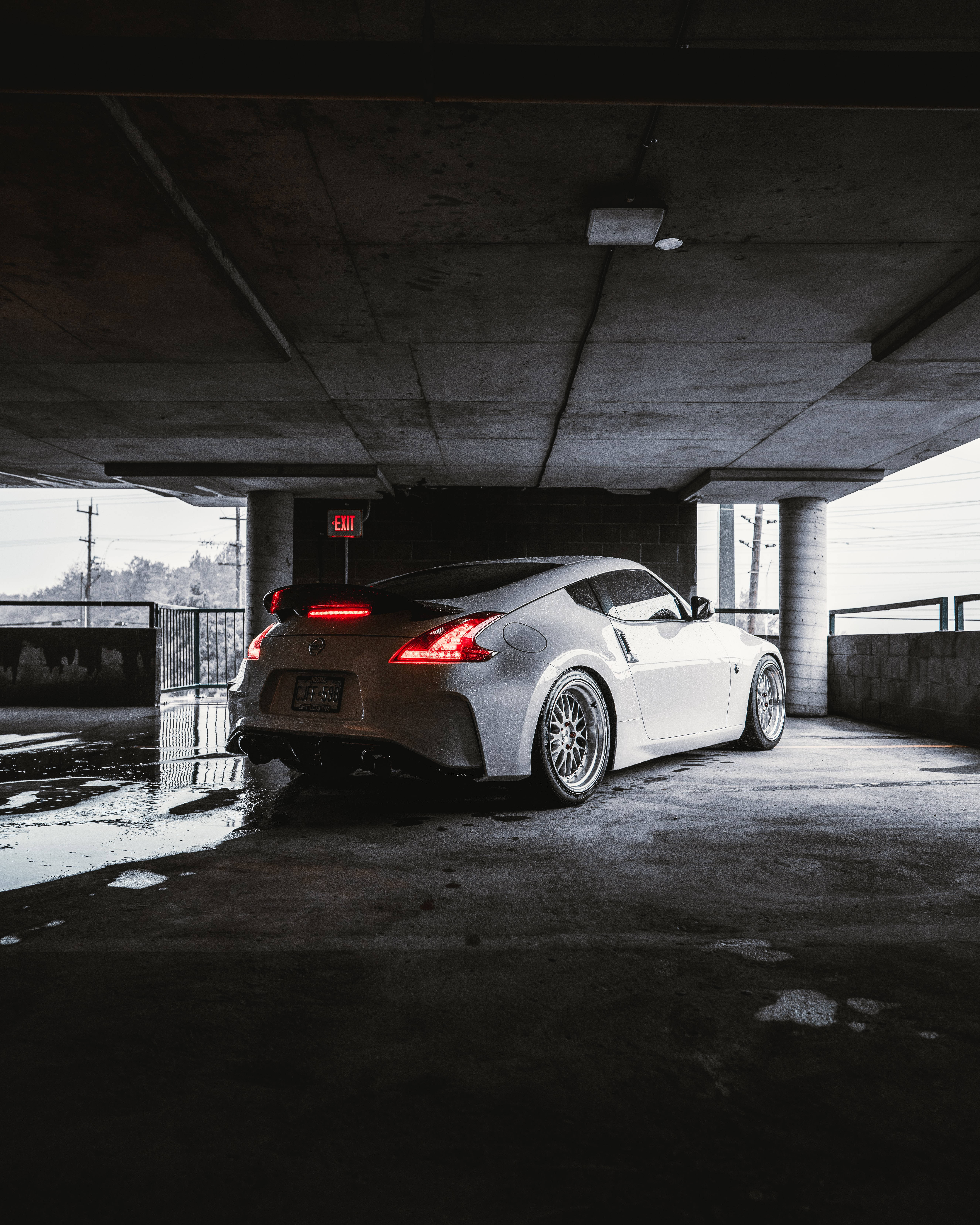 Nissan 桌布 壁紙 — 一輛時尚的白色跑車，紅色尾燈發光，停泊在濕漉漉的混凝土天橋下，黃昏時分。
