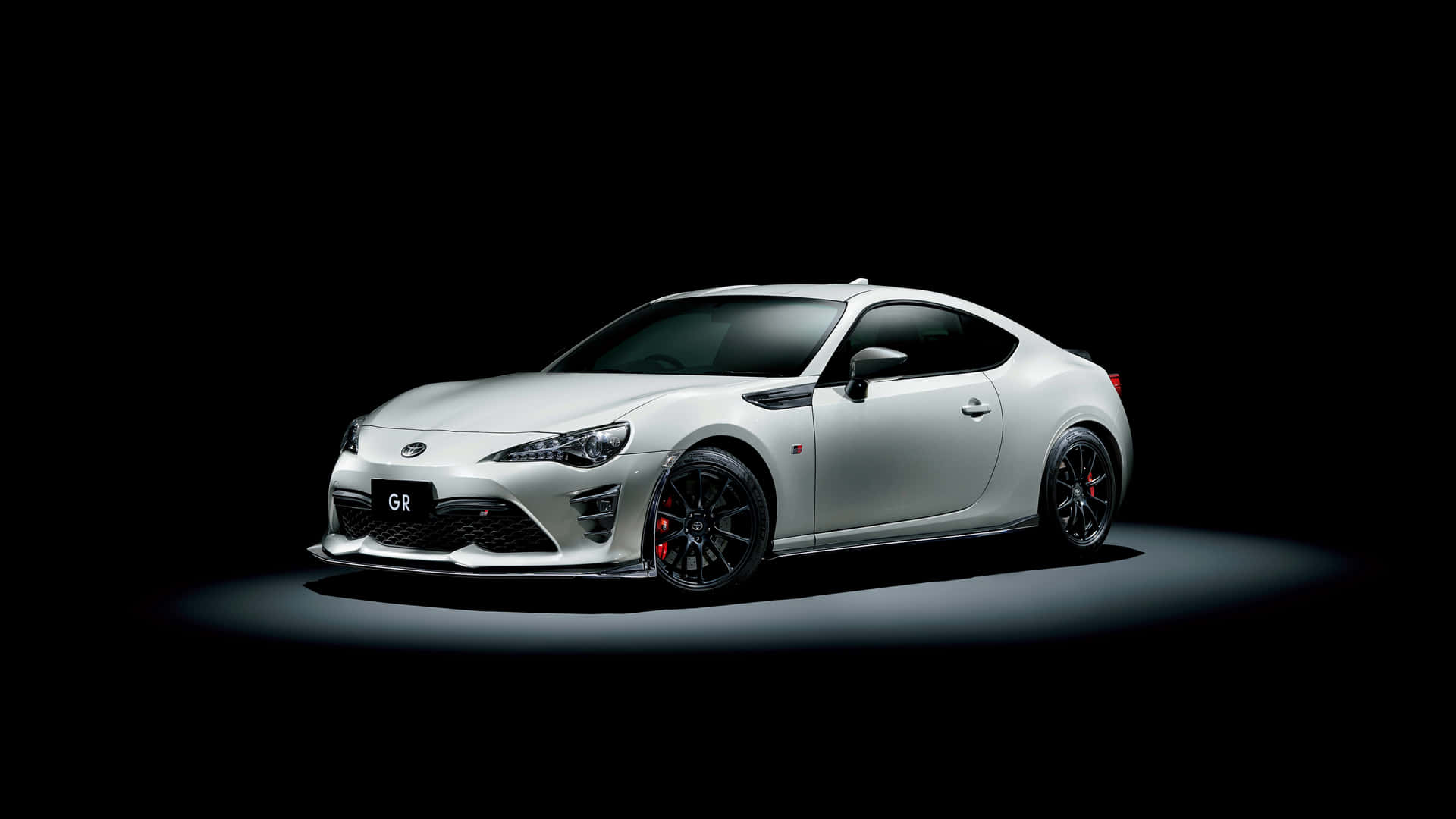 白色跑車配備黑色輪圈和紅色制動器，在黑暗工作室中照亮。 — Toyota Supra Mk4 壁紙