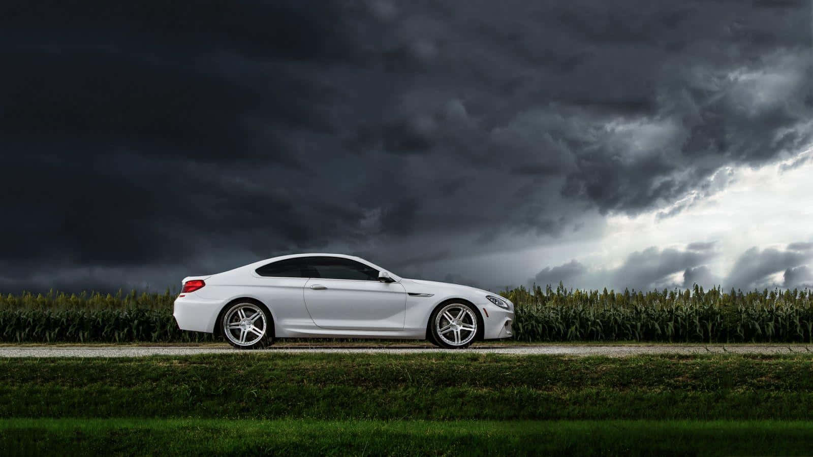 Bmw 6 Series 桌布 壁紙 — 一輛時尚的白色跑車停泊在鄉村道路上，頭頂上是戲劇性的暴風雨天空，烏雲密佈。