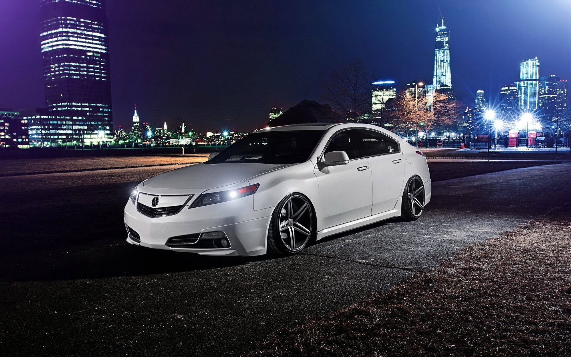 Acura 桌布 壁紙 — 一輛時尚的白色跑車在城市的燈光下閃閃發光，映襯著充滿活力的夜景天際線和明亮的摩天大樓。