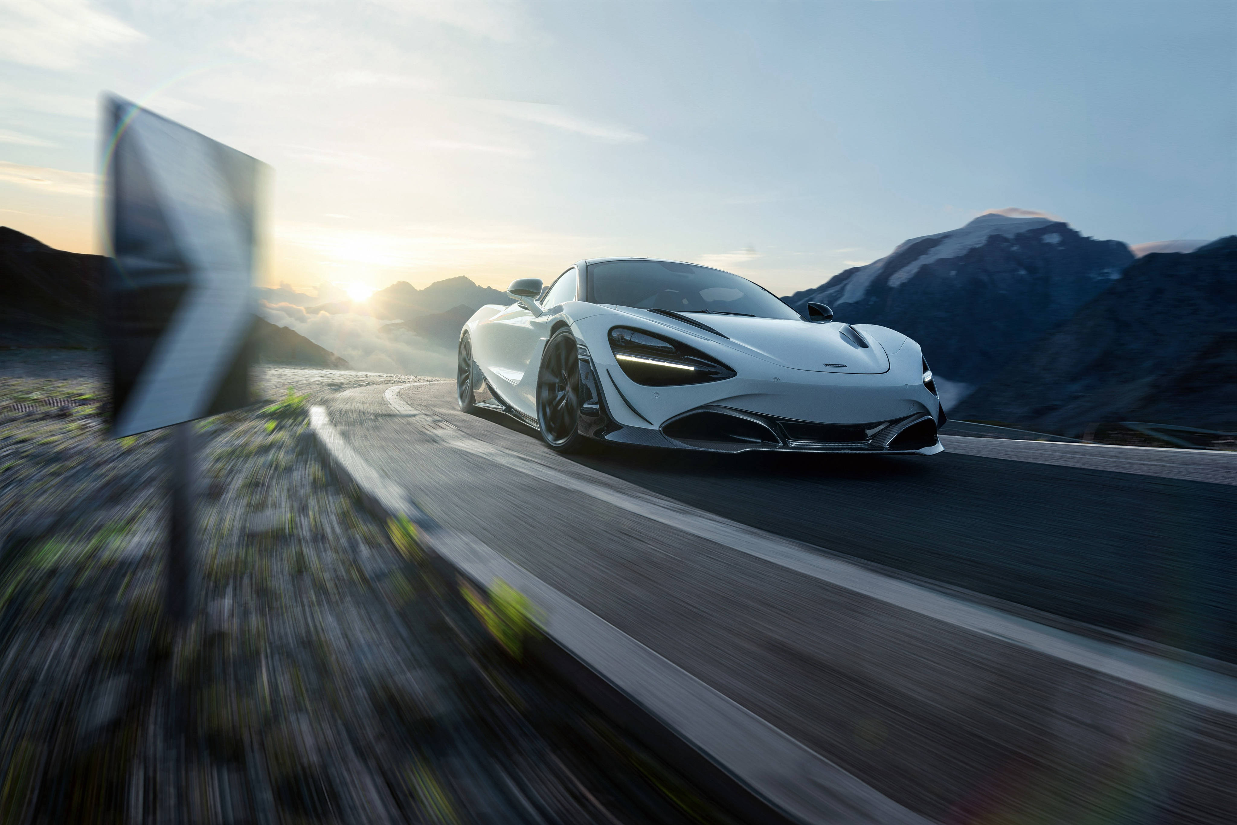 Mclaren 720s 桌布 壁紙 — 一輛時尚的白色跑車在日出時沿著蜿蜒的山路疾馳，背景是白雪覆蓋的山峰，帶有模糊的動感效果。