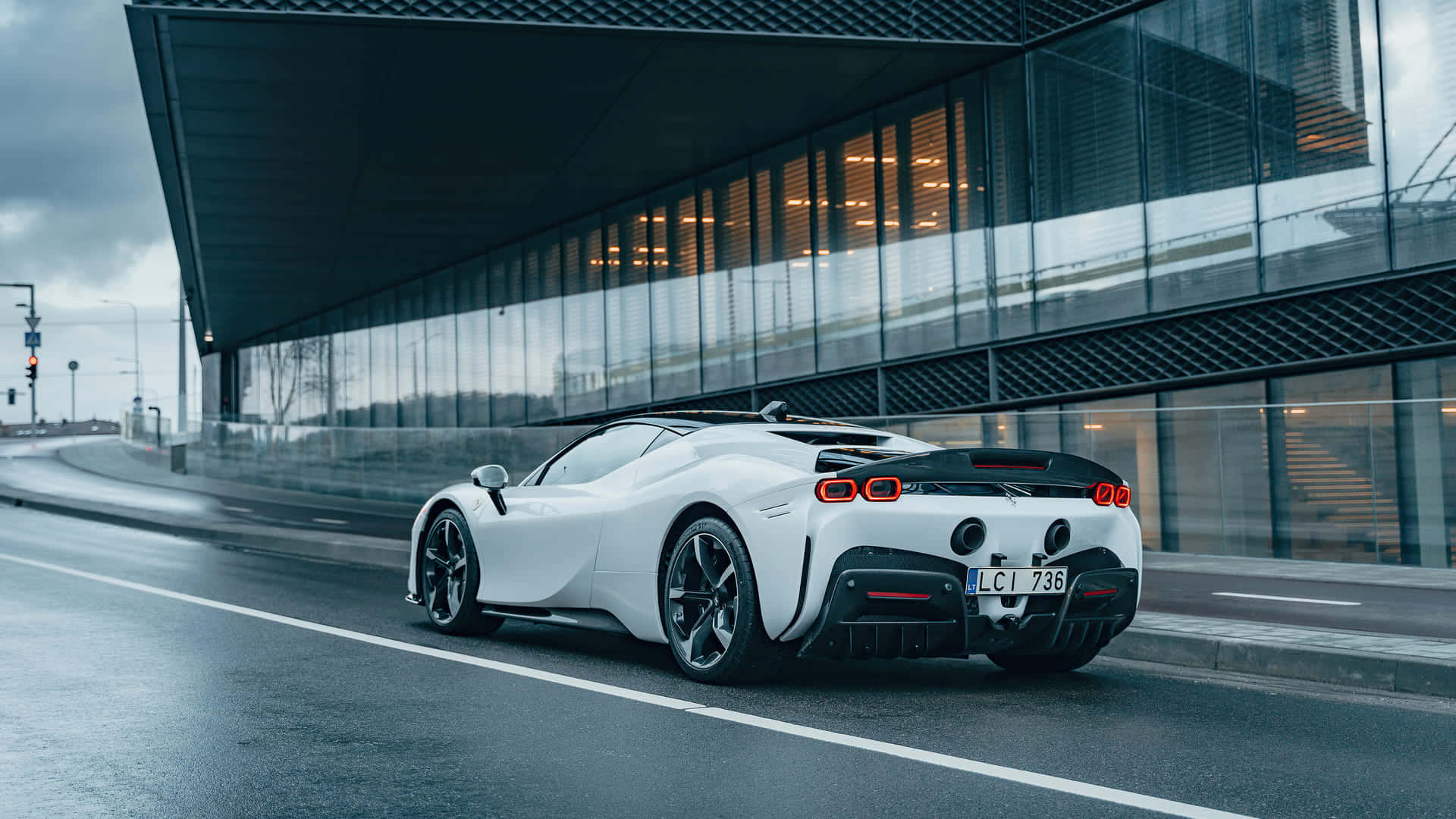 1920 X 1080 Car 桌布 壁紙 — 一輛時尚的白色跑車帶有發光的紅色尾燈，在陰天下行駛在潮濕的城市道路上，旁邊是一座現代玻璃建築。