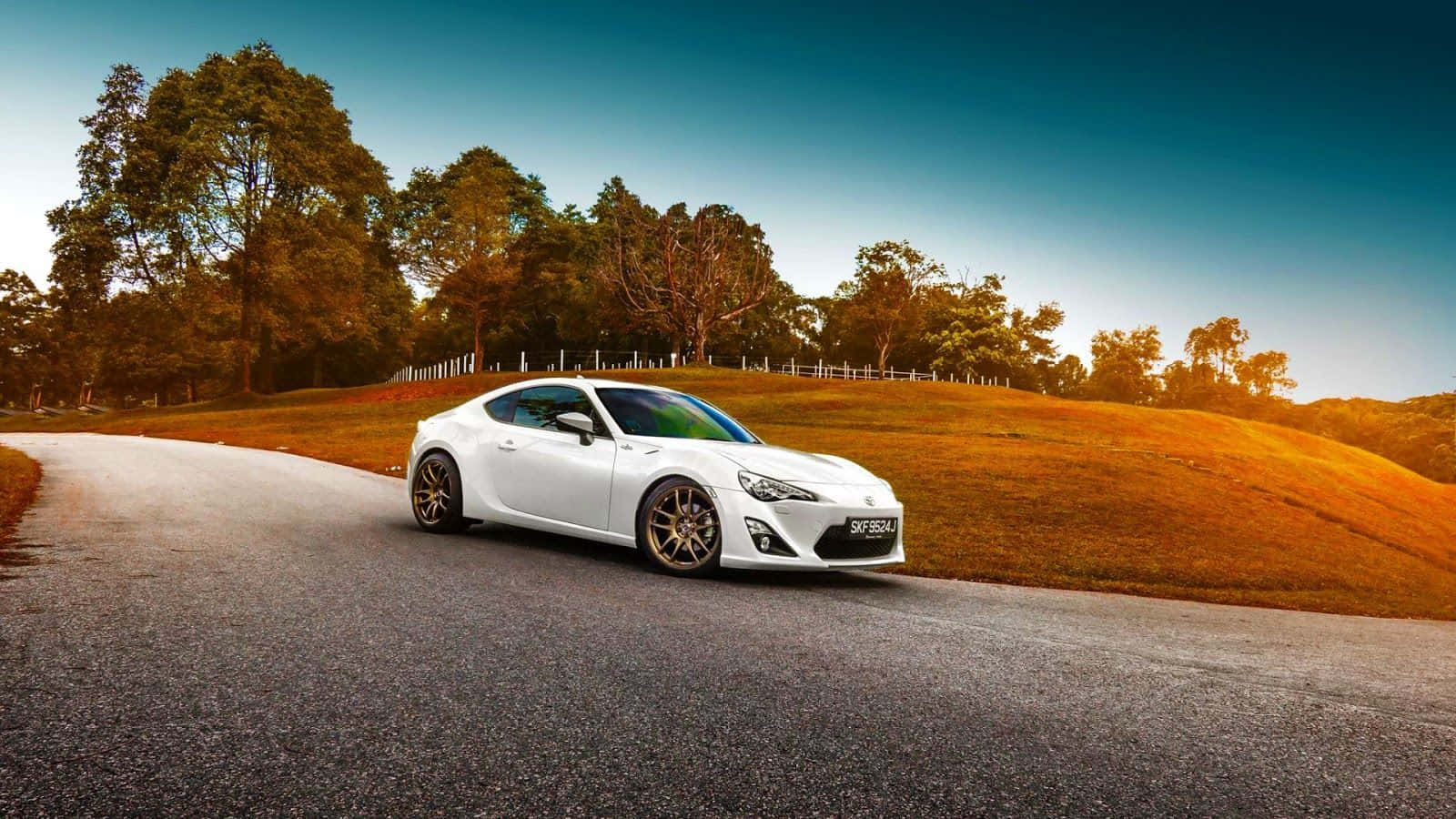 白色跑車在蜿蜒的道路上行駛，穿過日落時分的金色山丘。 — Toyota Supra Mk4 壁紙