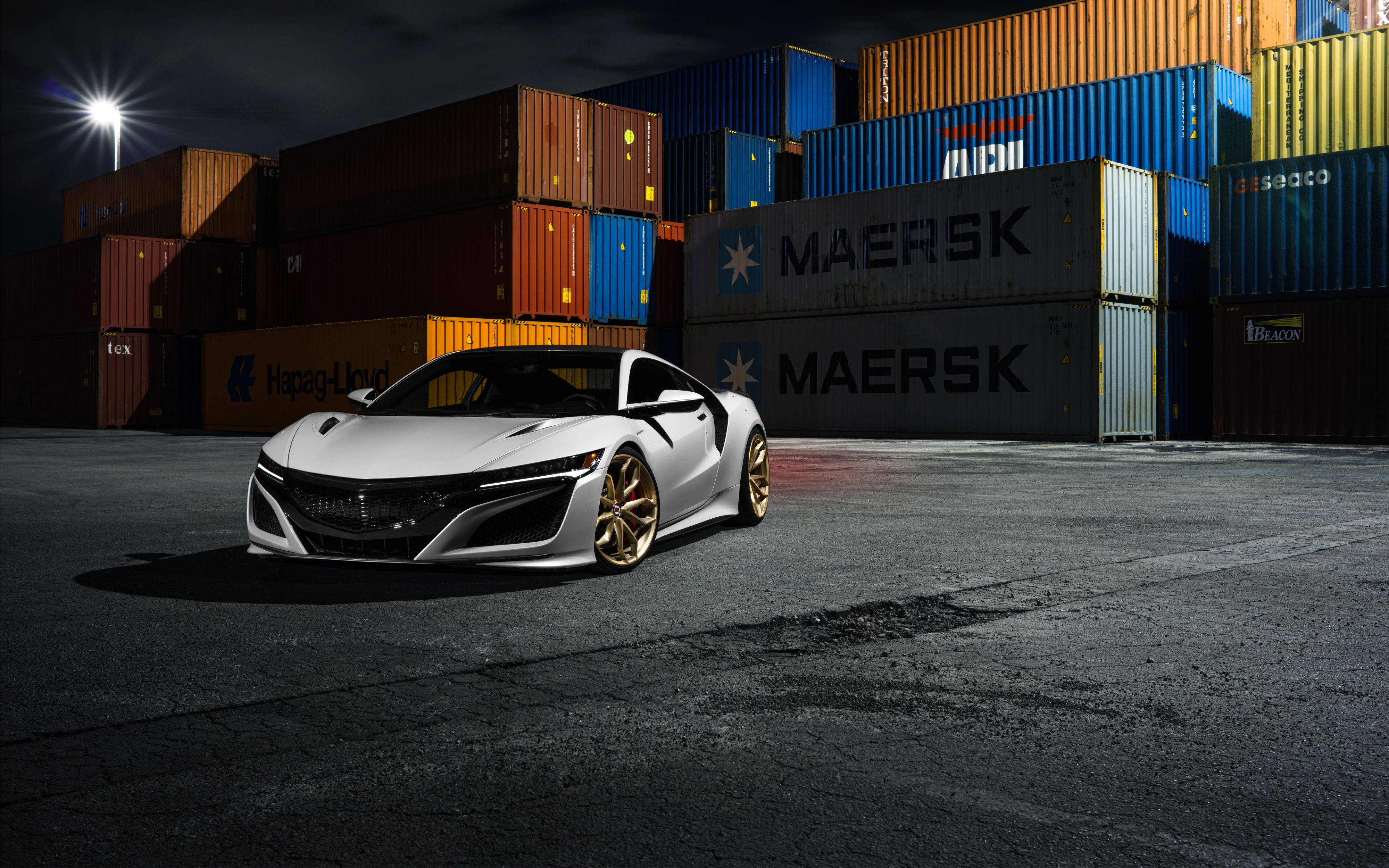 Acura 桌布 壁紙 — 一輛時尚的白色跑車配金色輪圈，夜間停放在堆疊的貨運集裝箱之間，在明亮的聚光燈下。