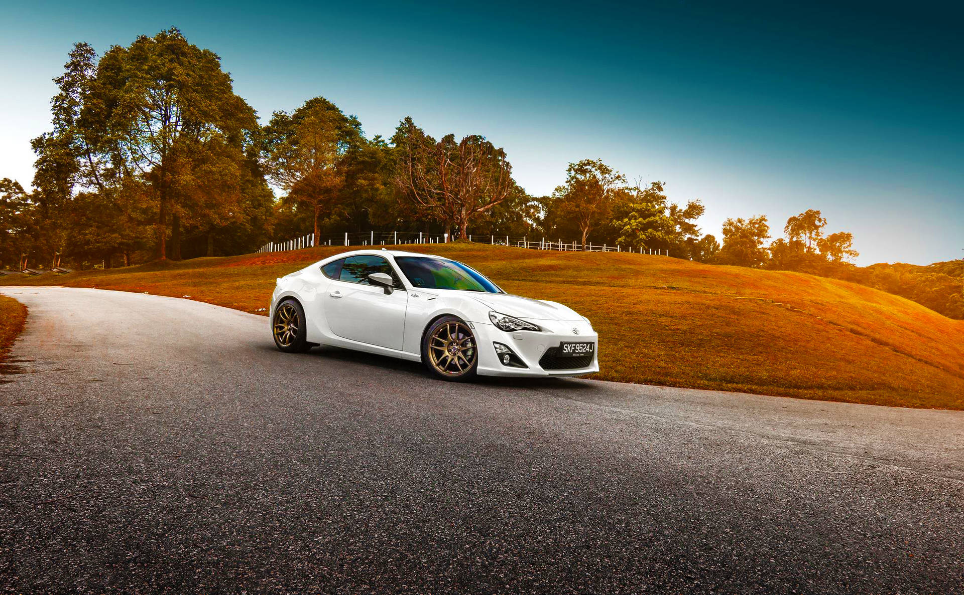 白色跑車配金色輪圈，在夕陽下穿過金色山丘的蜿蜒道路上。 — Toyota Supra Mk4 壁紙