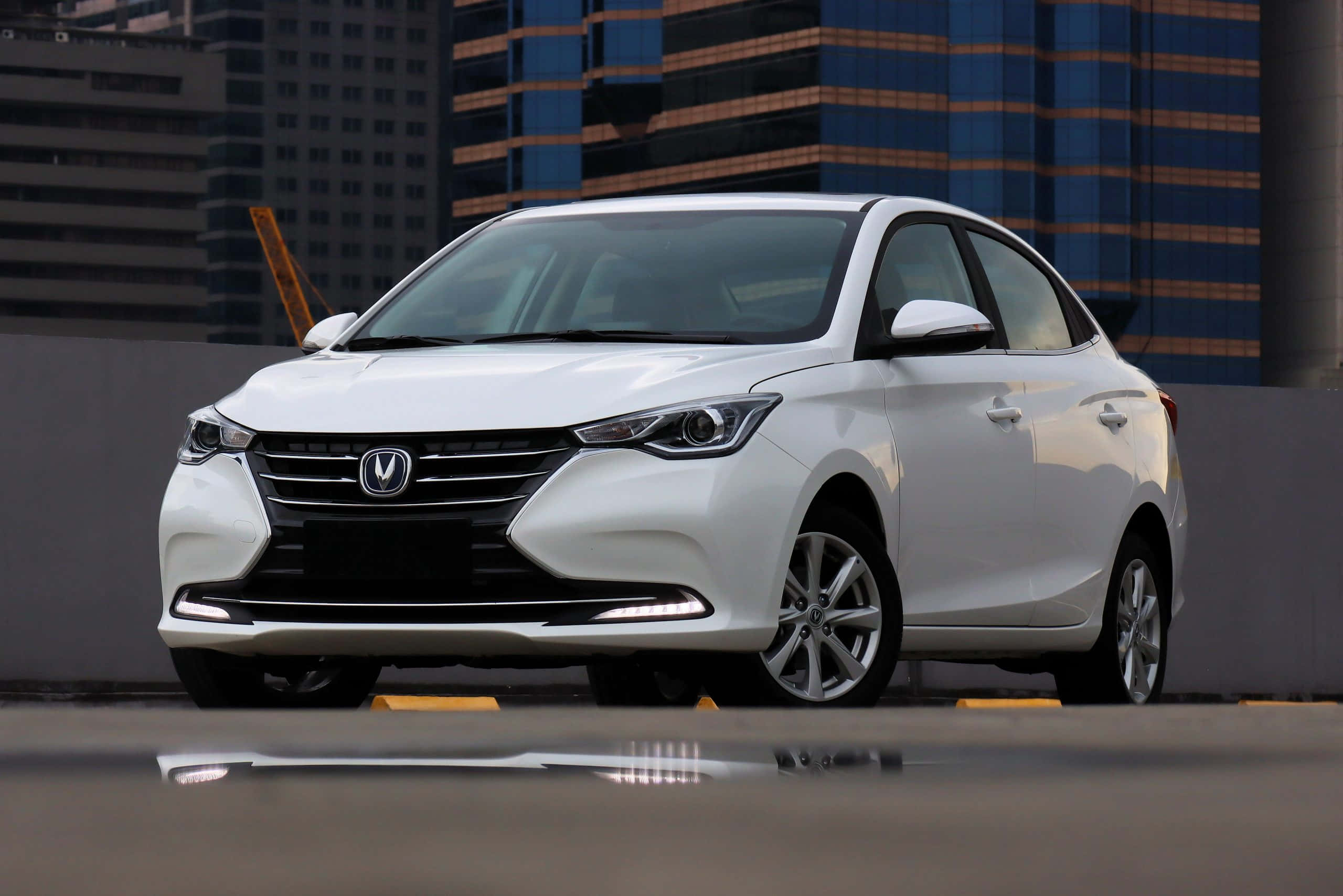Changan 桌布 壁紙 — 一輛時尚的白色轎車停泊在濕漉漉的城市屋頂上，背後現代摩天大樓倒映在水窪中。