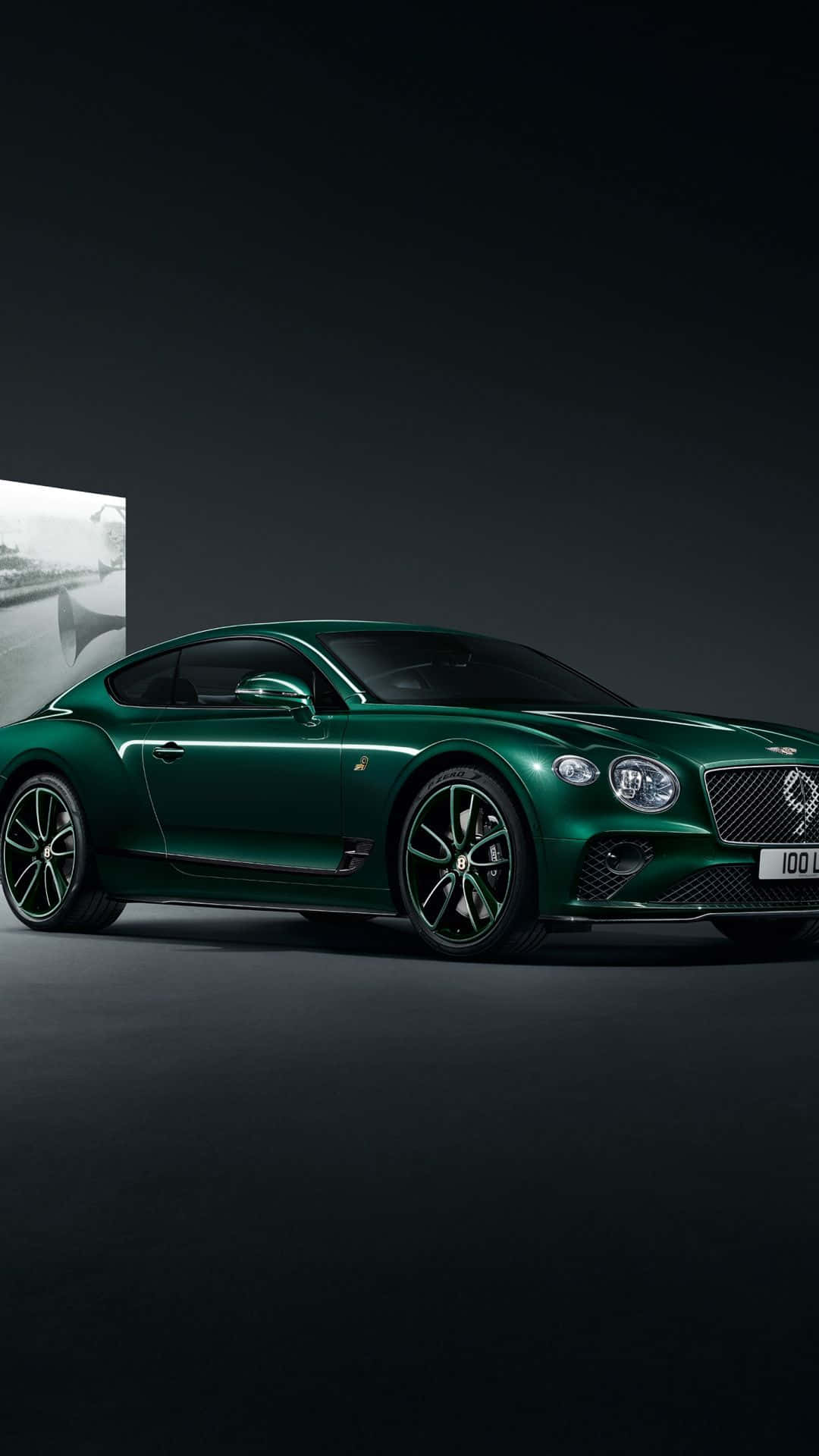 bentley HD 桌布 壁紙 — 一輛時尚的祖母綠賓利 Continental GT 雙門轎跑車在攝影棚燈光下閃閃發光，背景是深色牆壁上的黑白照片。