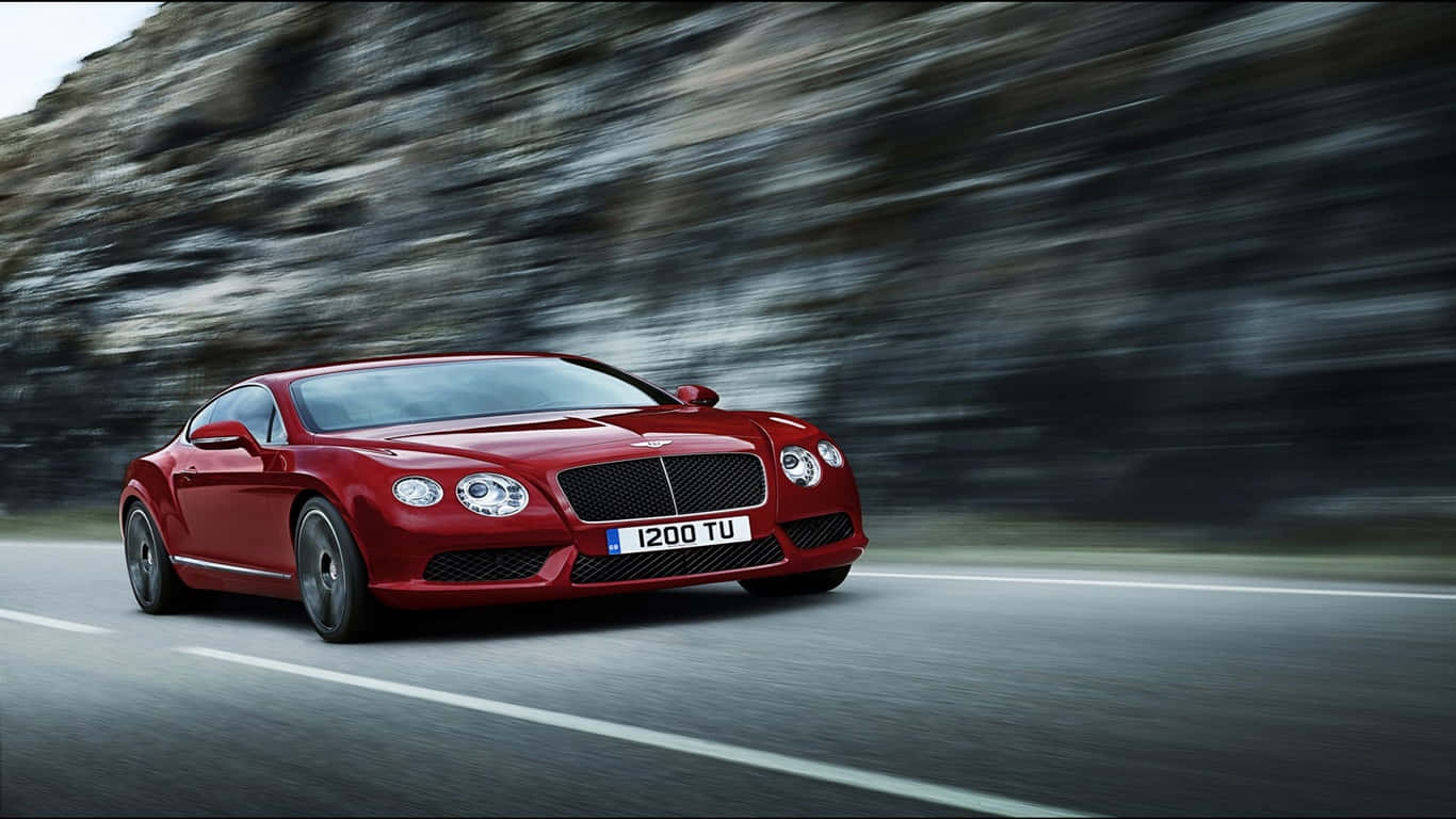 1366x768 Bentley 桌布 壁紙 — 一輛時尚的紅色 Bentley Continental GT 在蜿蜒的山路上疾馳，模糊的岩石峭壁呼嘯而過。