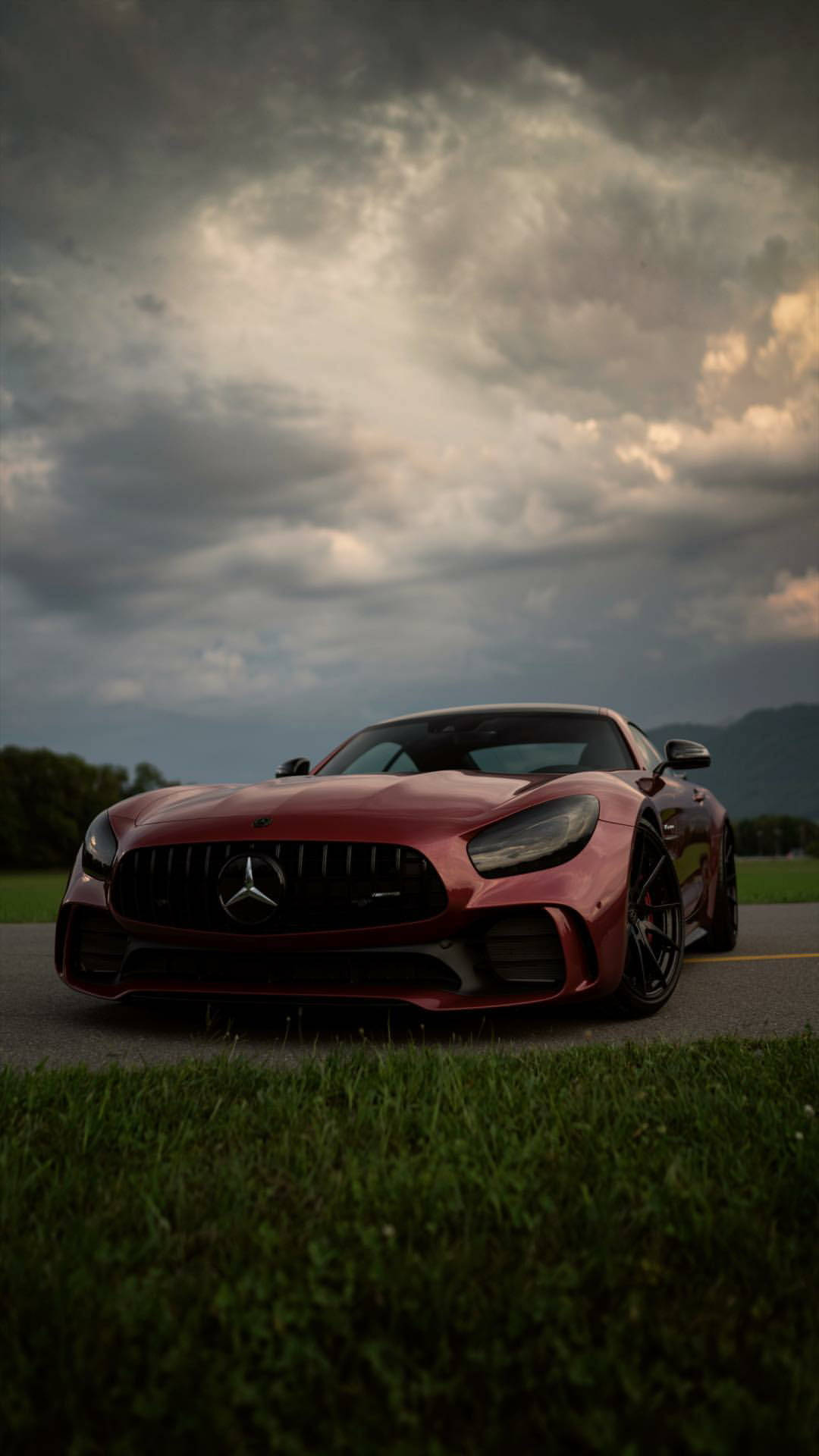 X 桌布 壁紙 — 一輛時尚的紅色 Mercedes-AMG GT 停泊在道路上，天空烏雲密佈，前景有綠草。