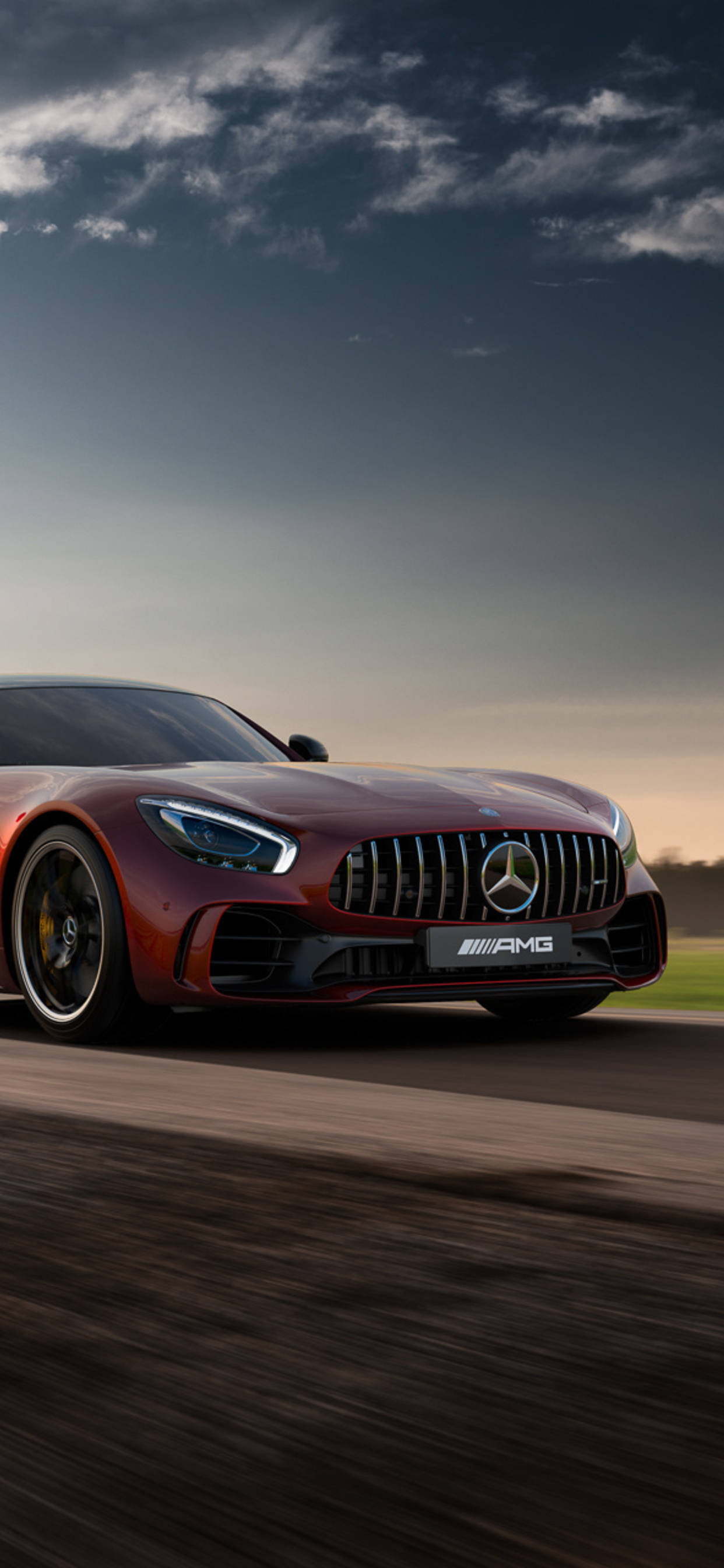 amg iPhone 桌布 壁紙 — 一輛時尚的紅色 Mercedes-AMG GT 跑車在模糊的道路上奔馳，背景是戲劇性的暮色天空。