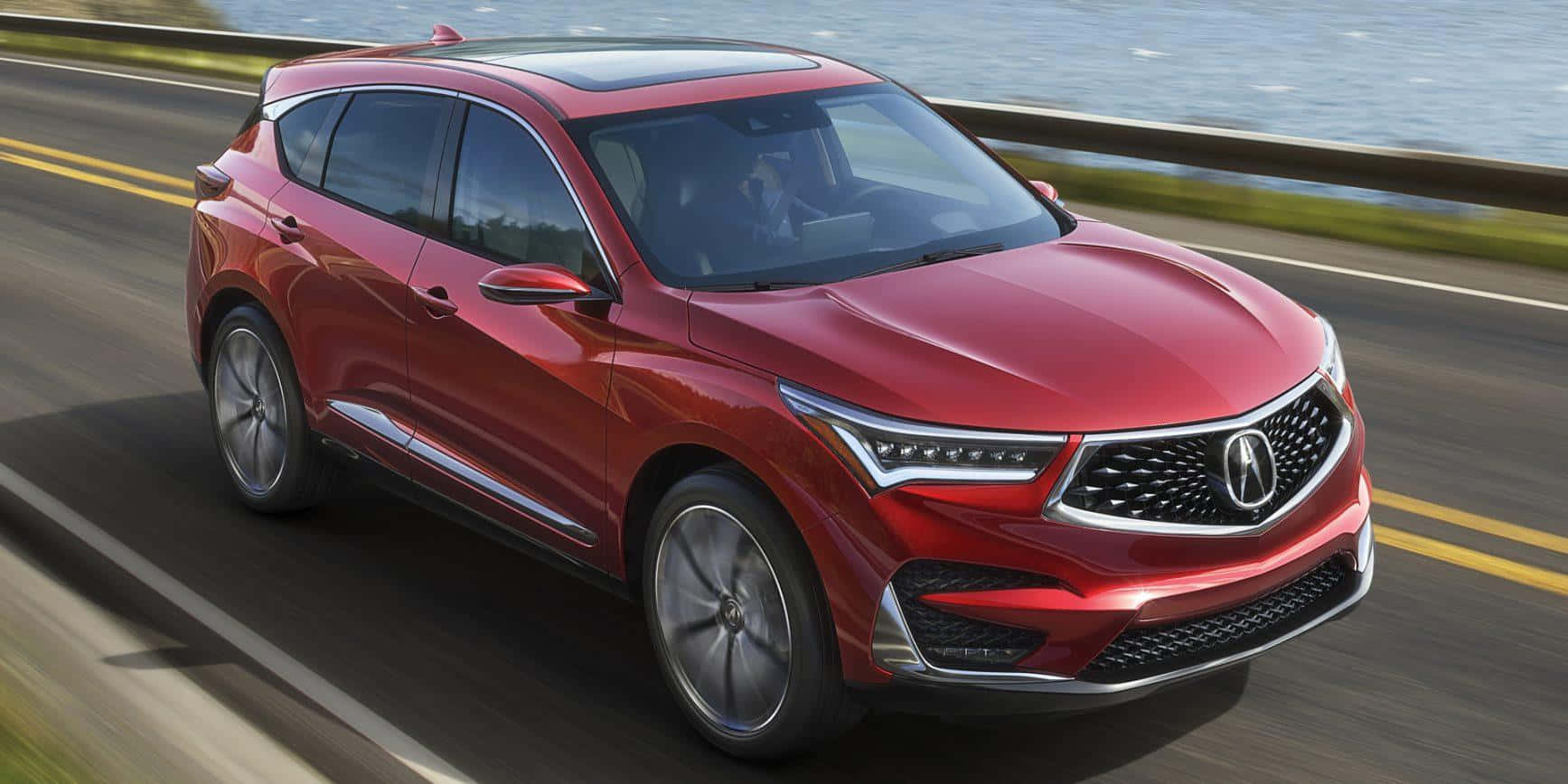 Acura Mdx 桌布 壁紙 — 一輛時尚的紅色Acura SUV沿著沿海高速公路行駛，背景是模糊的水面和綠植。