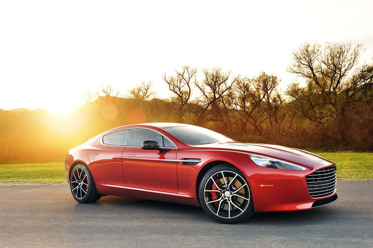 Aston Martin Rapide S 桌布 壁紙 — 一輛時尚的紅色Aston Martin跑車在金色日落時分，以光禿禿的樹木為背景，在道路上閃閃發光。