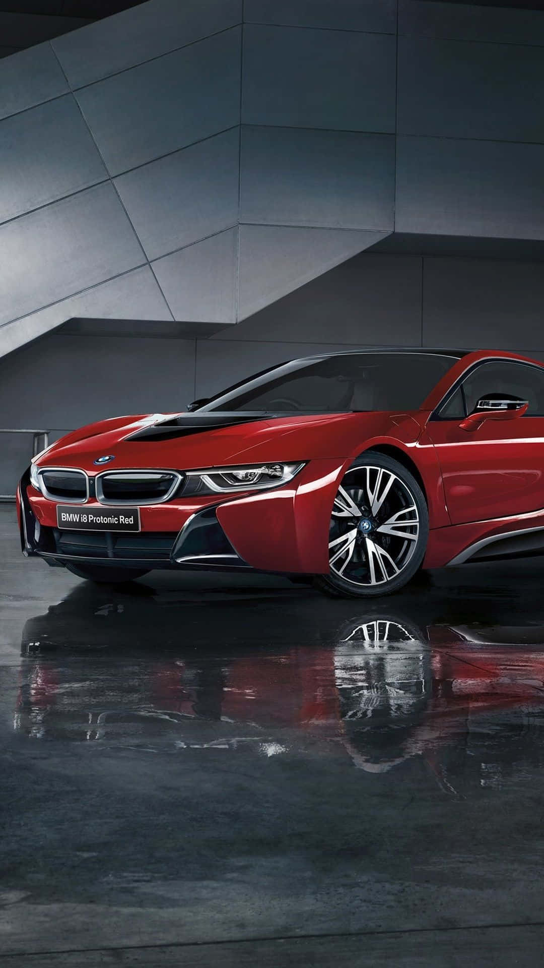 桌布 壁紙 — 一輛時尚的紅色BMW i8跑車在攝影棚燈光下閃耀，其倒影在濕潤的拋光地板上閃爍，背景是現代有棱角的灰色牆壁。