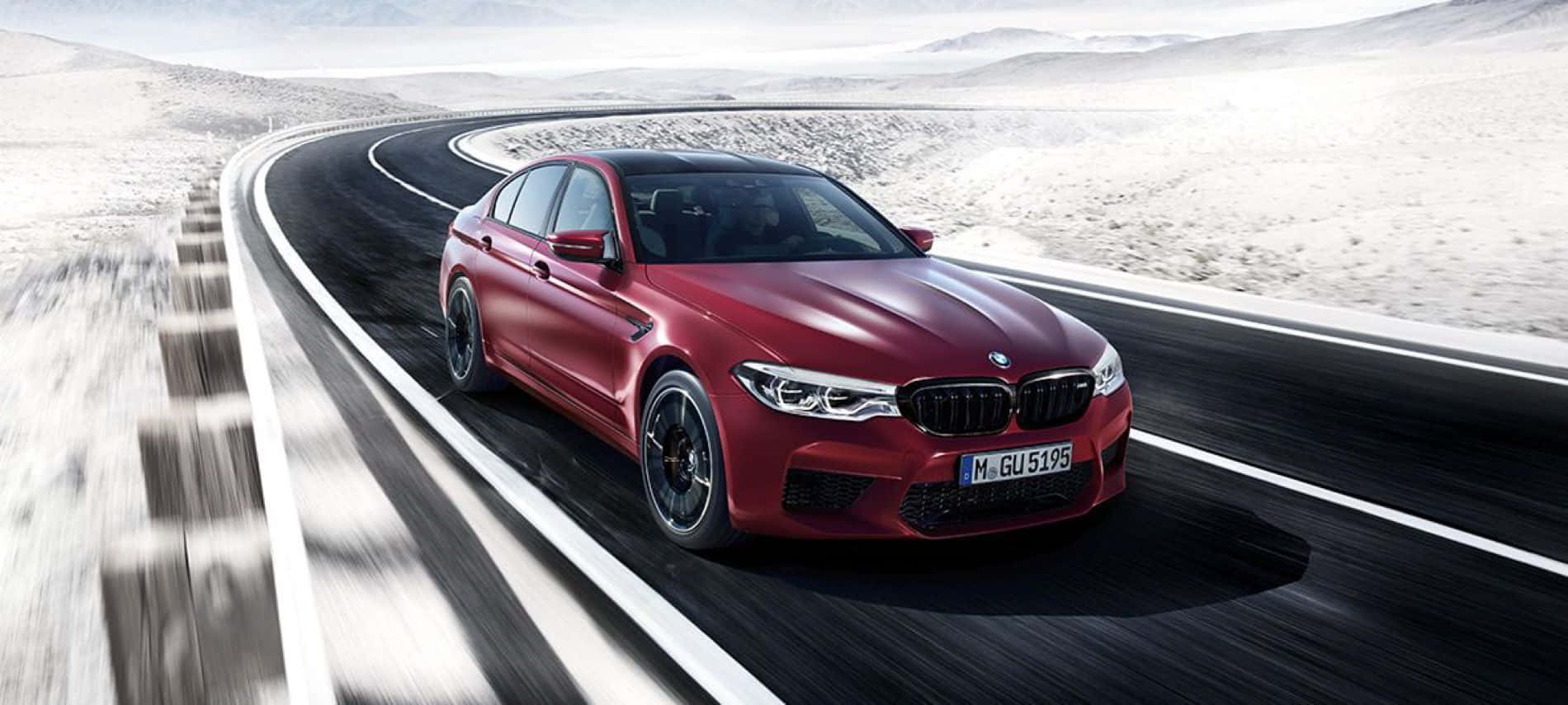 Bmw M5 桌布 壁紙 — 一輛時尚的紅色BMW M5在明亮的天空下，沿著蜿蜒的沙漠高速公路疾馳，帶有模糊的動態和遠山。