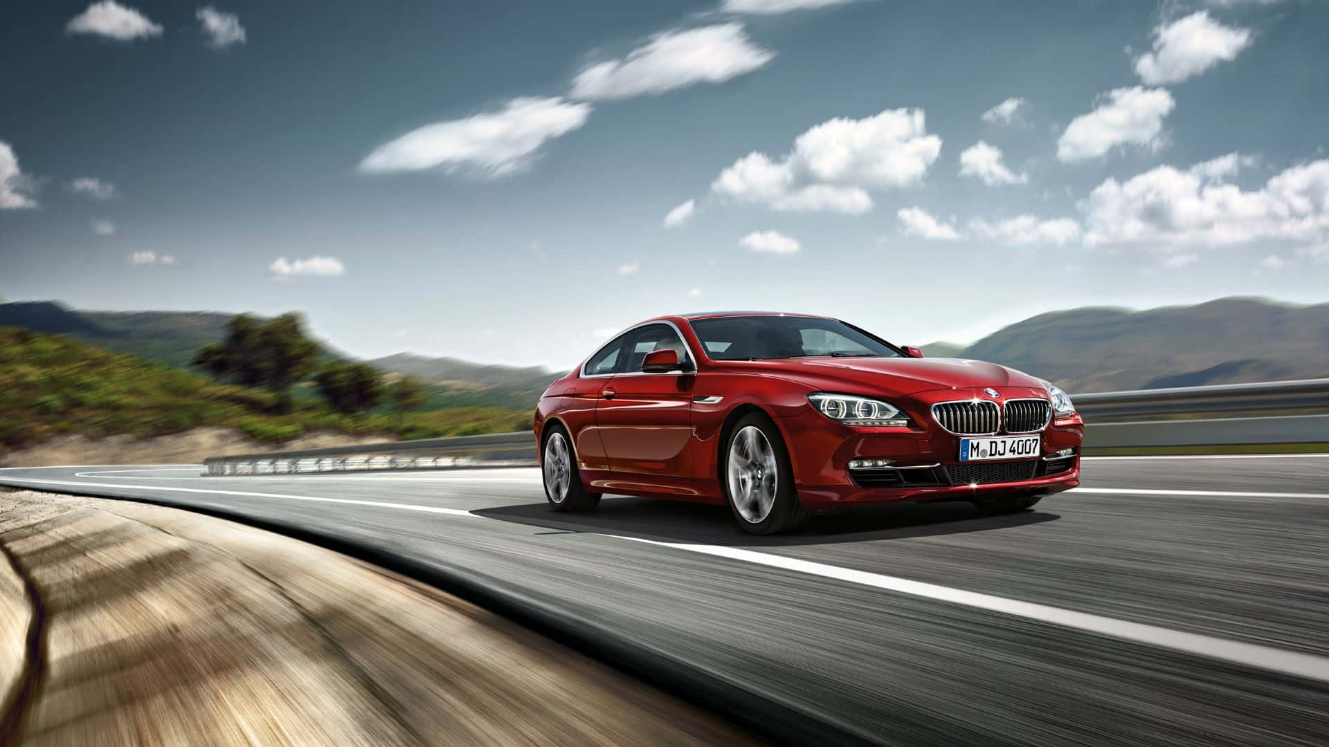 Bmw 6 Series 桌布 壁紙 — 一輛時尚的紅色BMW雙門跑車在晴朗藍天和蓬鬆白雲下，沿著蜿蜒的山路飛馳。