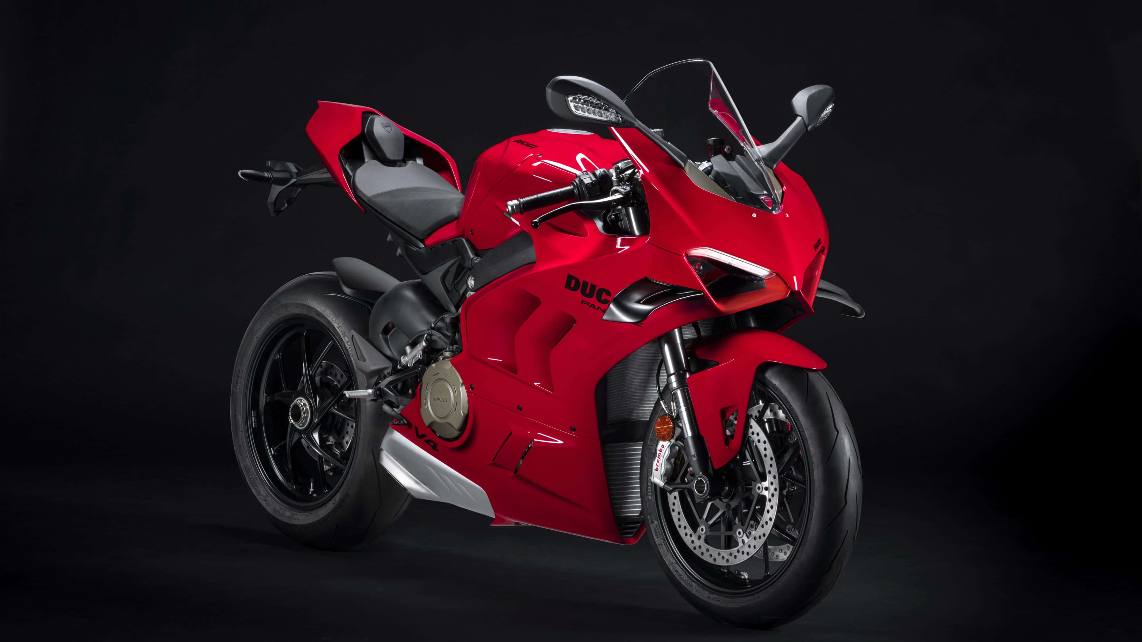 4K Bikes 桌布 壁紙 — 一輛時尚的紅色Ducati機車，帶有黑色點綴和銀色排氣管，在深色攝影棚背景前蓄勢待發。