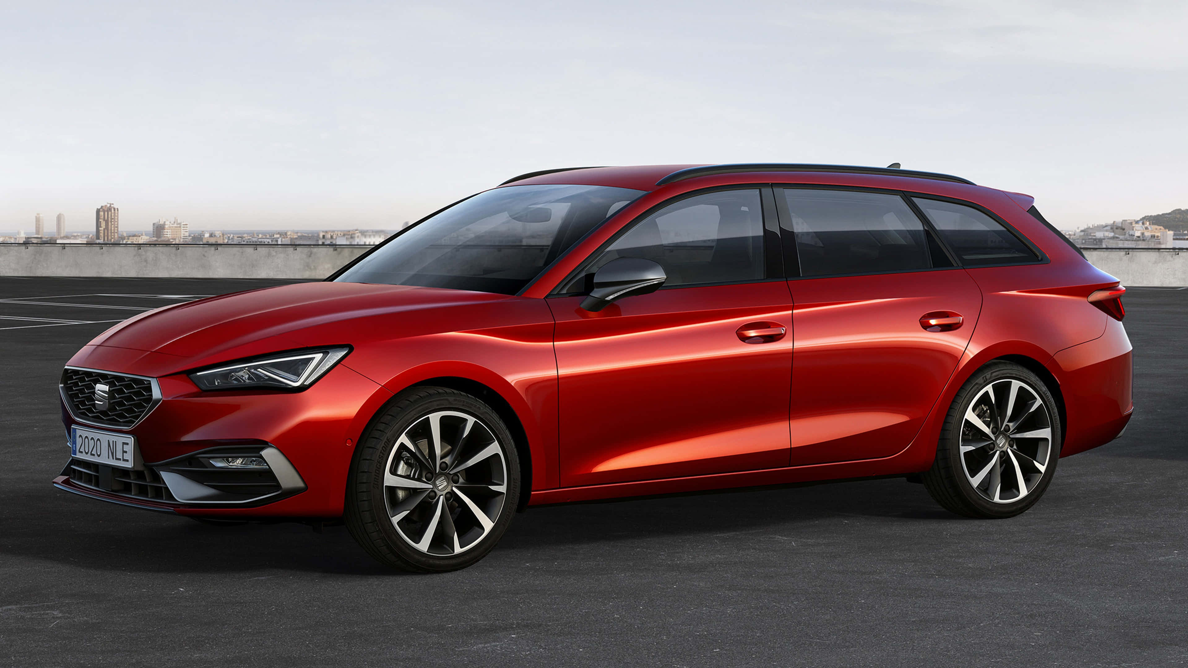 seat 桌布 壁紙 — 一輛時尚的紅色SEAT Leon旅行車停放在屋頂上，背景是城市天際線。