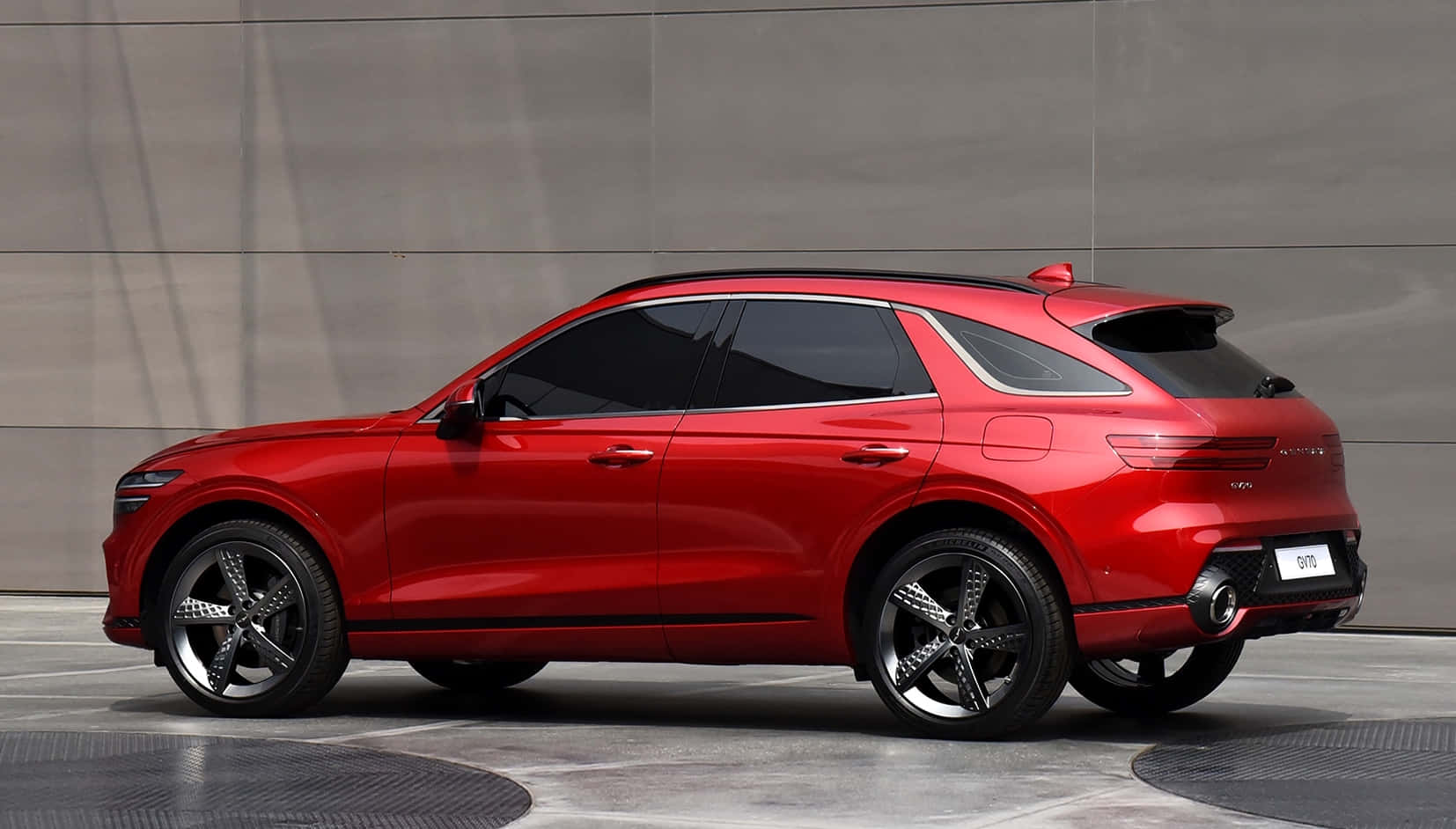 Genesis Gv70 桌布 壁紙 — 一輛時尚的紅色SUV，帶有黑色飾邊和時尚車輪，停在簡約的灰色混凝土牆前。