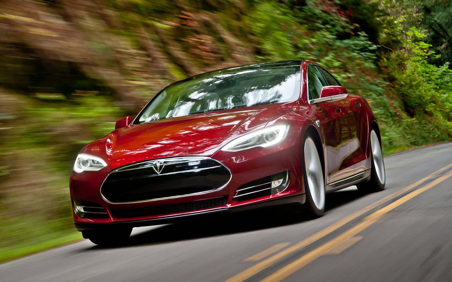 特斯拉 桌布 壁紙 — 一輛時尚的紅色Tesla Model S在蜿蜒的林間道路上疾馳，綠色樹葉呈現動態模糊效果。