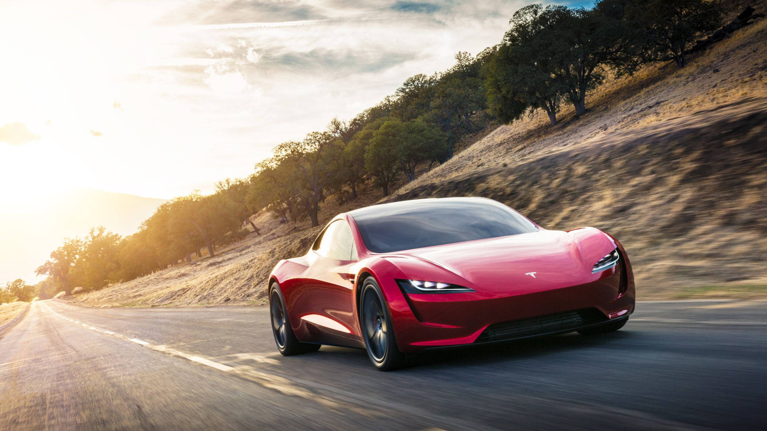 極高畫質 桌布 壁紙 — 一輛時尚的紅色Tesla Roadster在蜿蜒的鄉村道路上疾馳，沐浴在金色的夕陽光中。