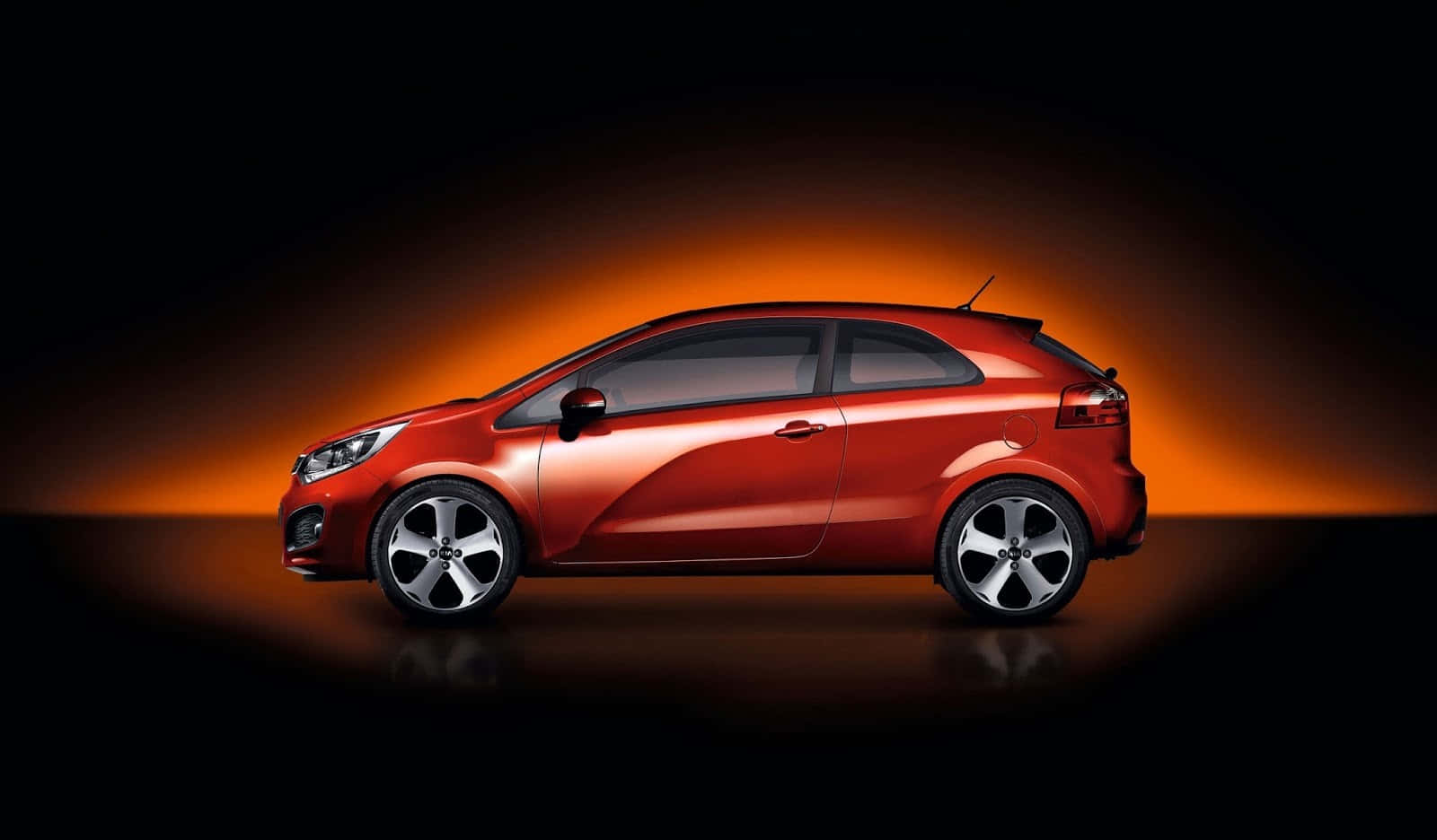 Best Car 桌布 壁紙 — 一輛時尚的紅色小型車在溫暖的橙色工作室燈光下，在深色背景中閃耀。